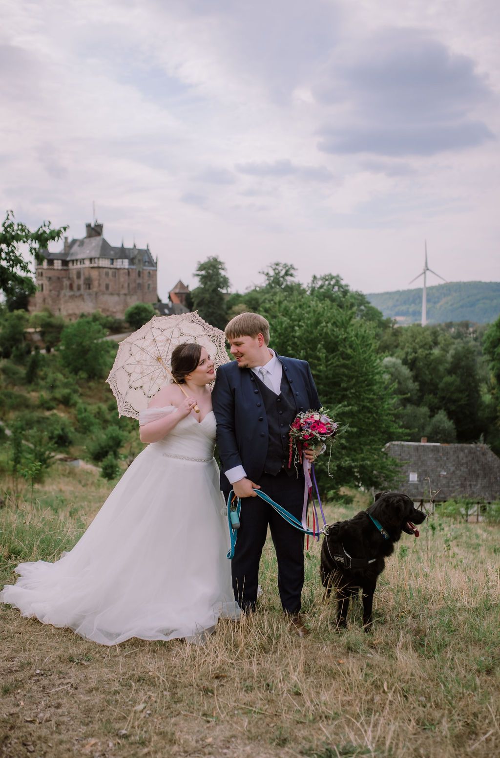 A bride and groom walking their dog on an open field during their small wedding in Germany