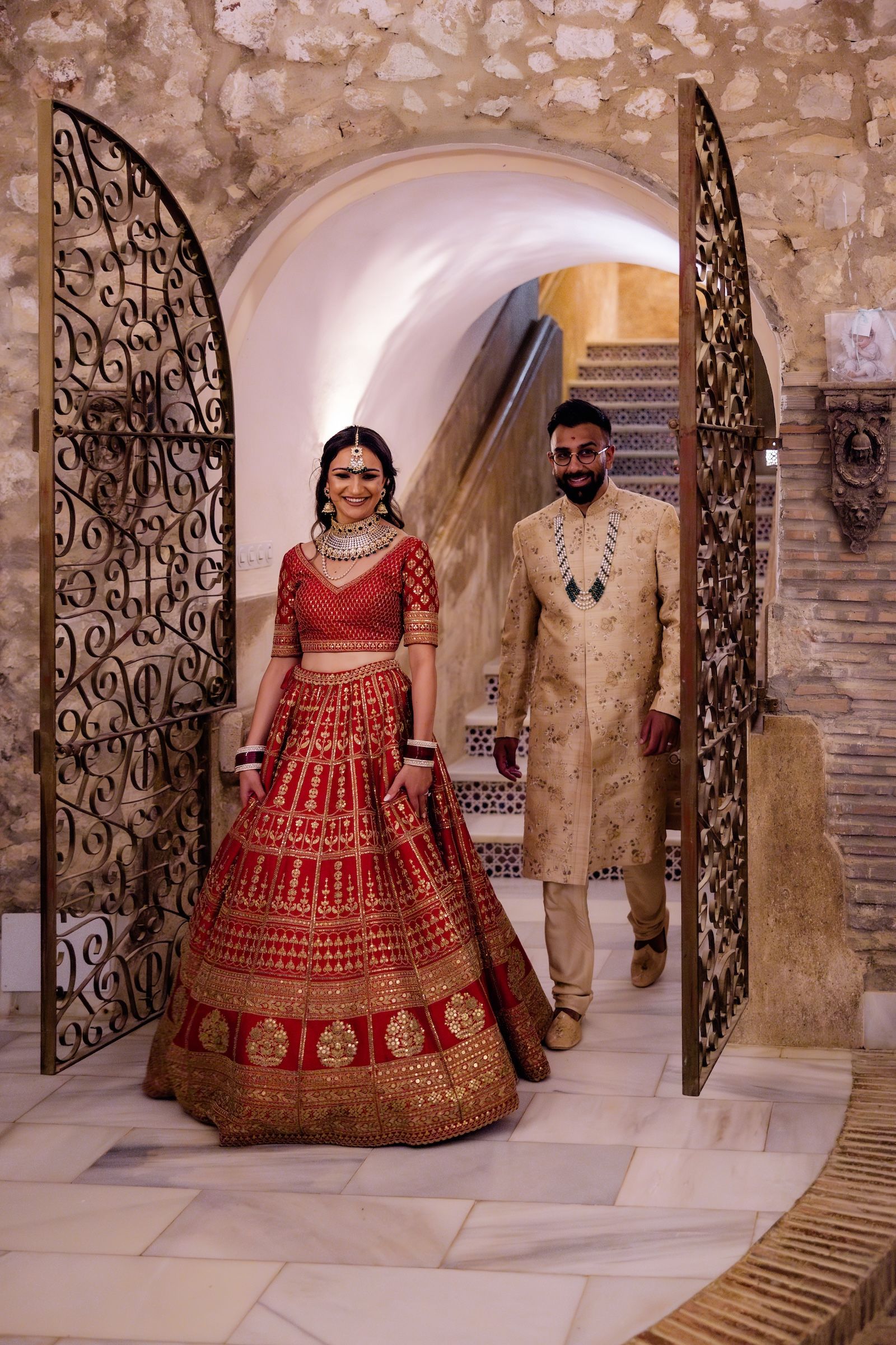A couple wearing Hindu wedding attire inside a medieval room during their destination wedding in Spain