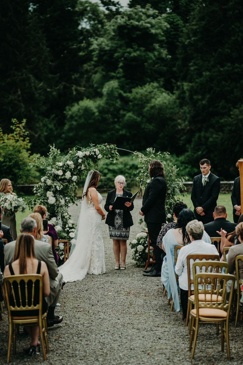 Bride and groom having an outdoor ceremony with a floral arch at the back for their intimate wedding in Ireland destination wedding in Ireland