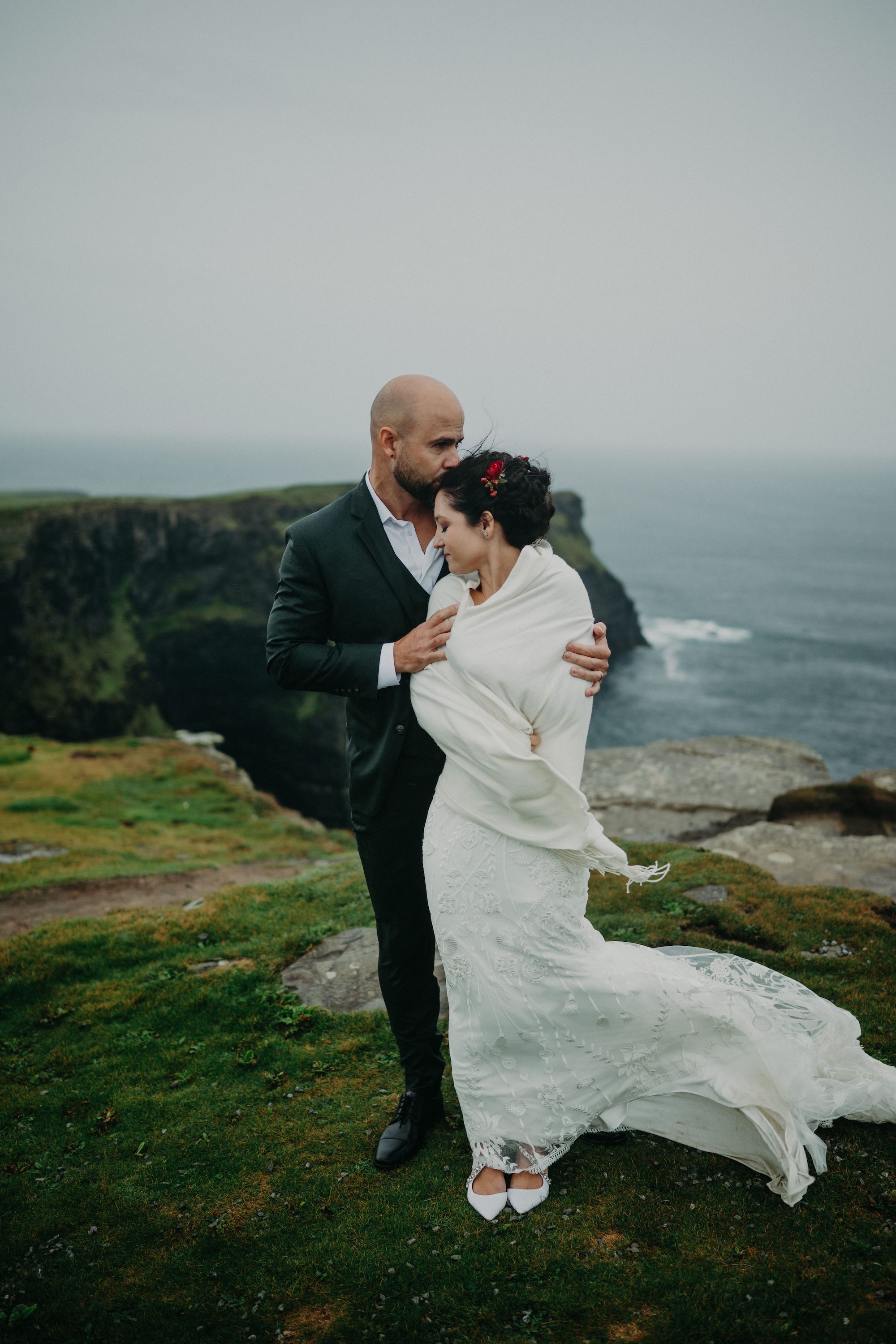 Bride and groom pose romantically atop the Cliffs of Moher for the photoshoot of their small wedding in Ireland