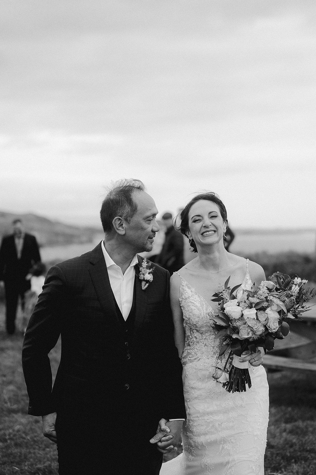Black and white photo of newlyweds on top of a cliff in Ireland with the bride laughing and holding her bouquet