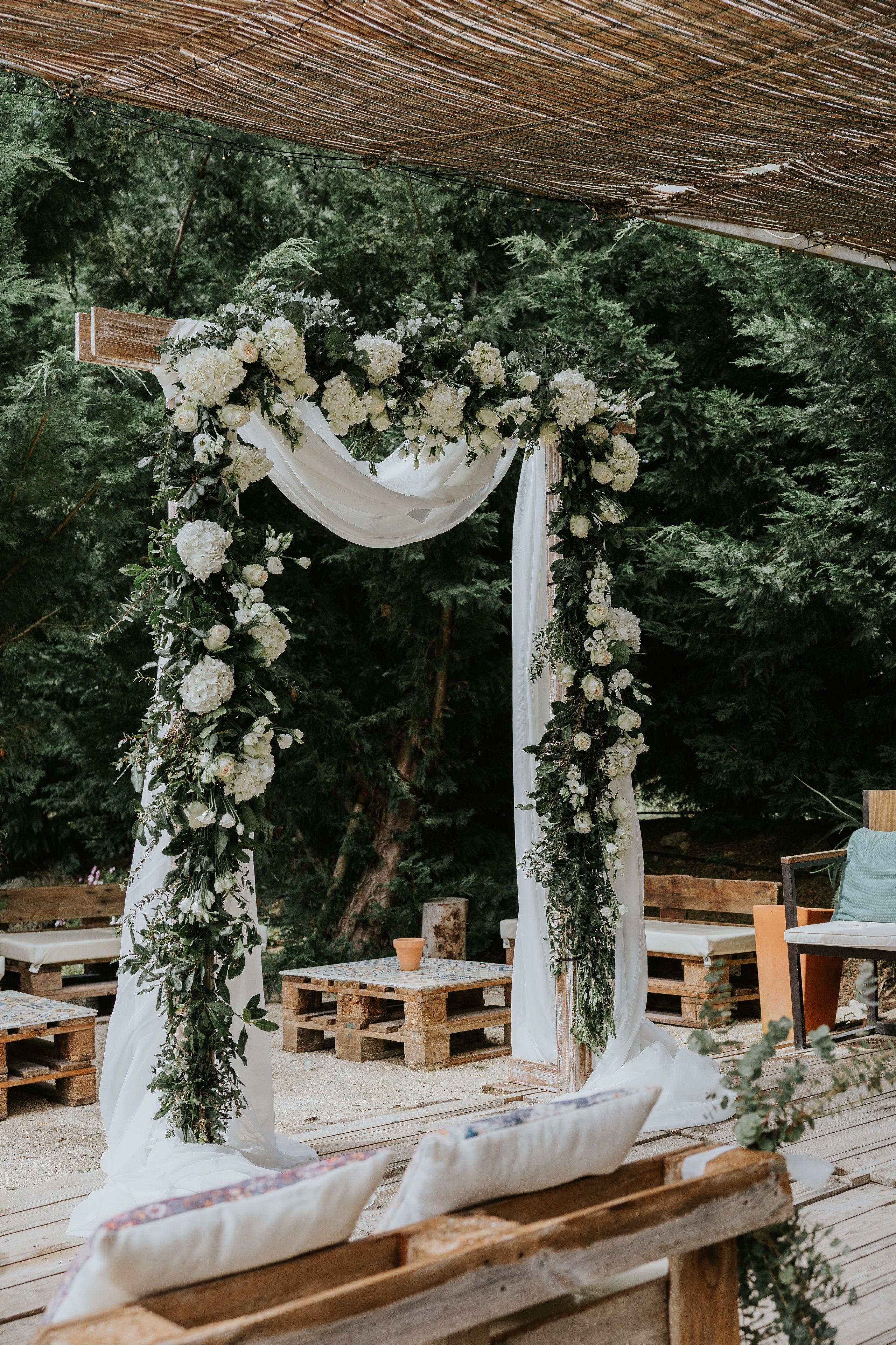 A rustic wooden wedding arch with white flowers and fresh greens