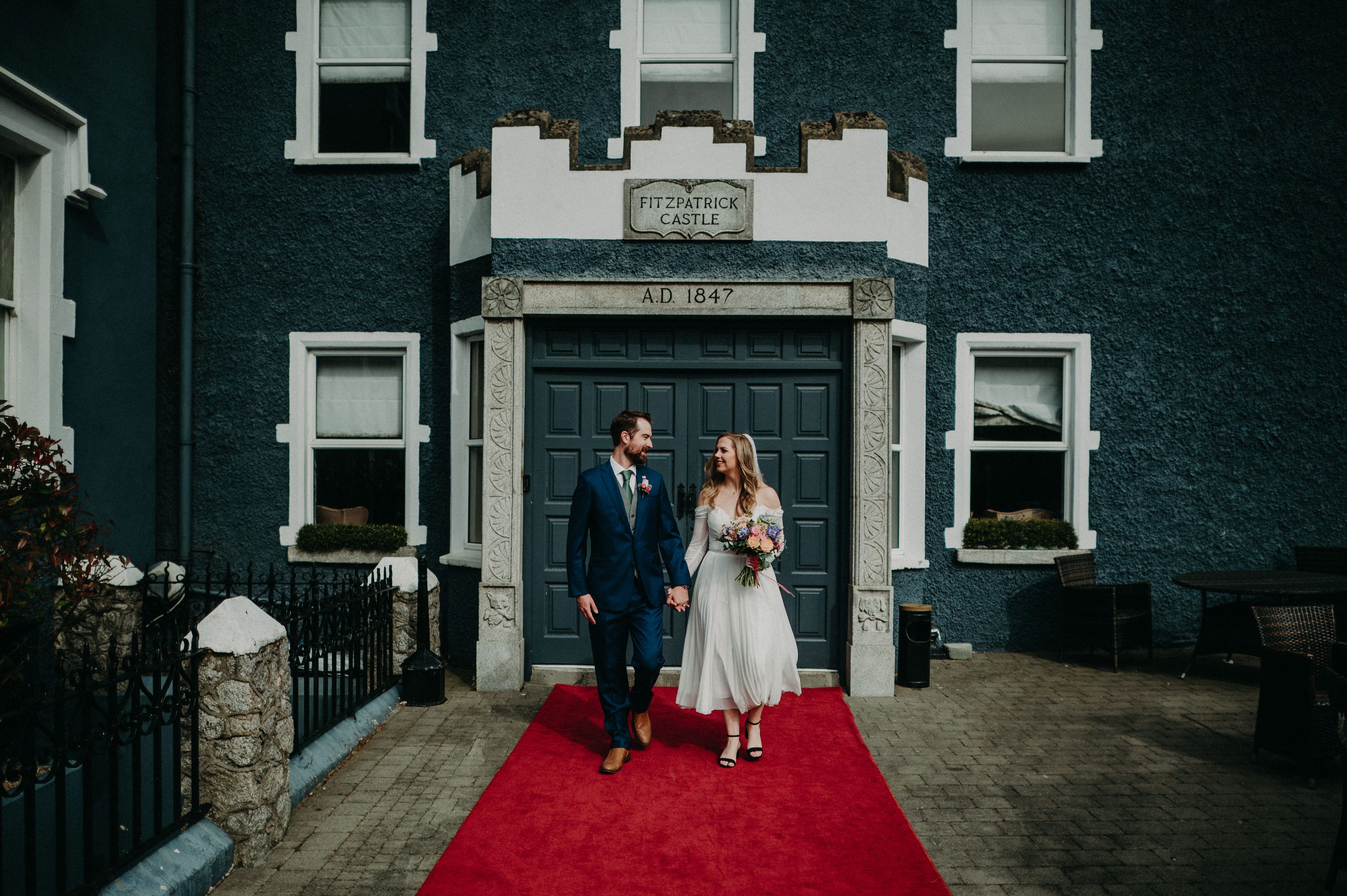 Bride and groom walking down the red carpet in front of a blue door of a castle during their Irish elopement