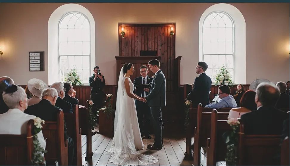 A wedding ceremony with the couple in front of guests inside a rustic chapel in Ireland 