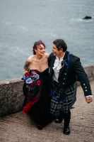 Bride who holds a purple and red bouquet, is with her groom, walking along a pathway in Slea Head with the ocean in the background