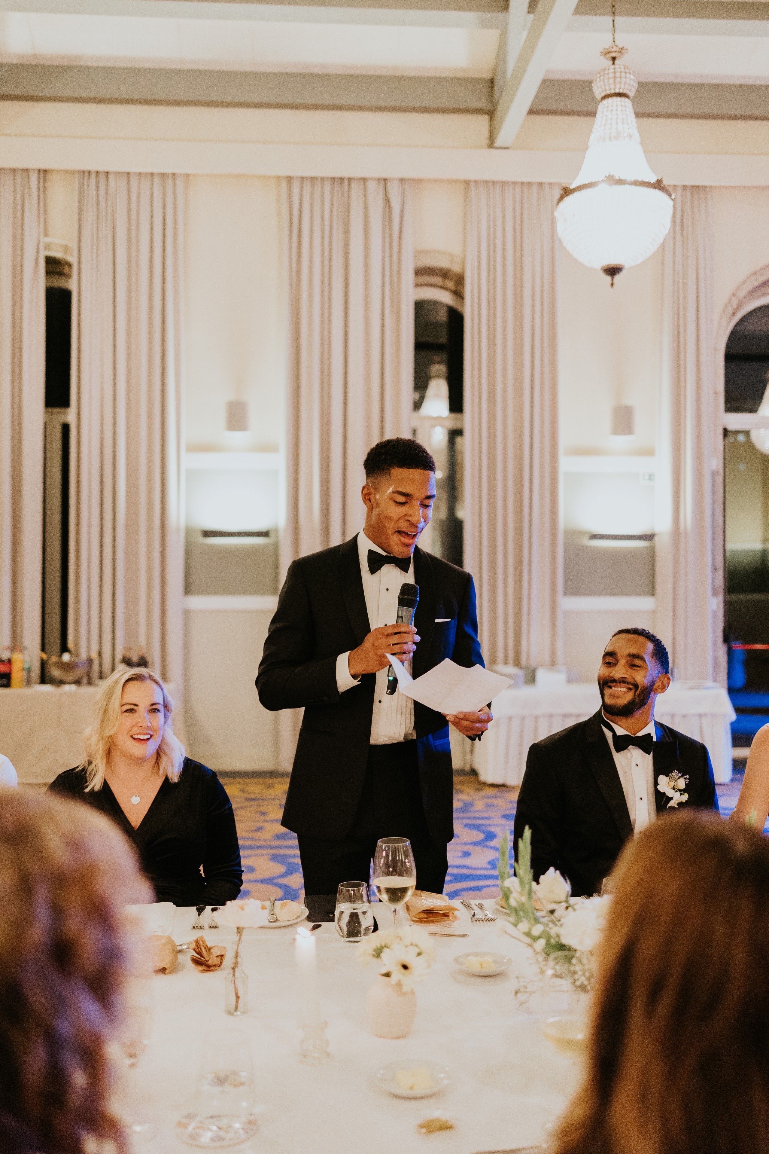 A guest at a wedding reception makes his speech while the groom beside him smiles during a destination wedding in Portugal