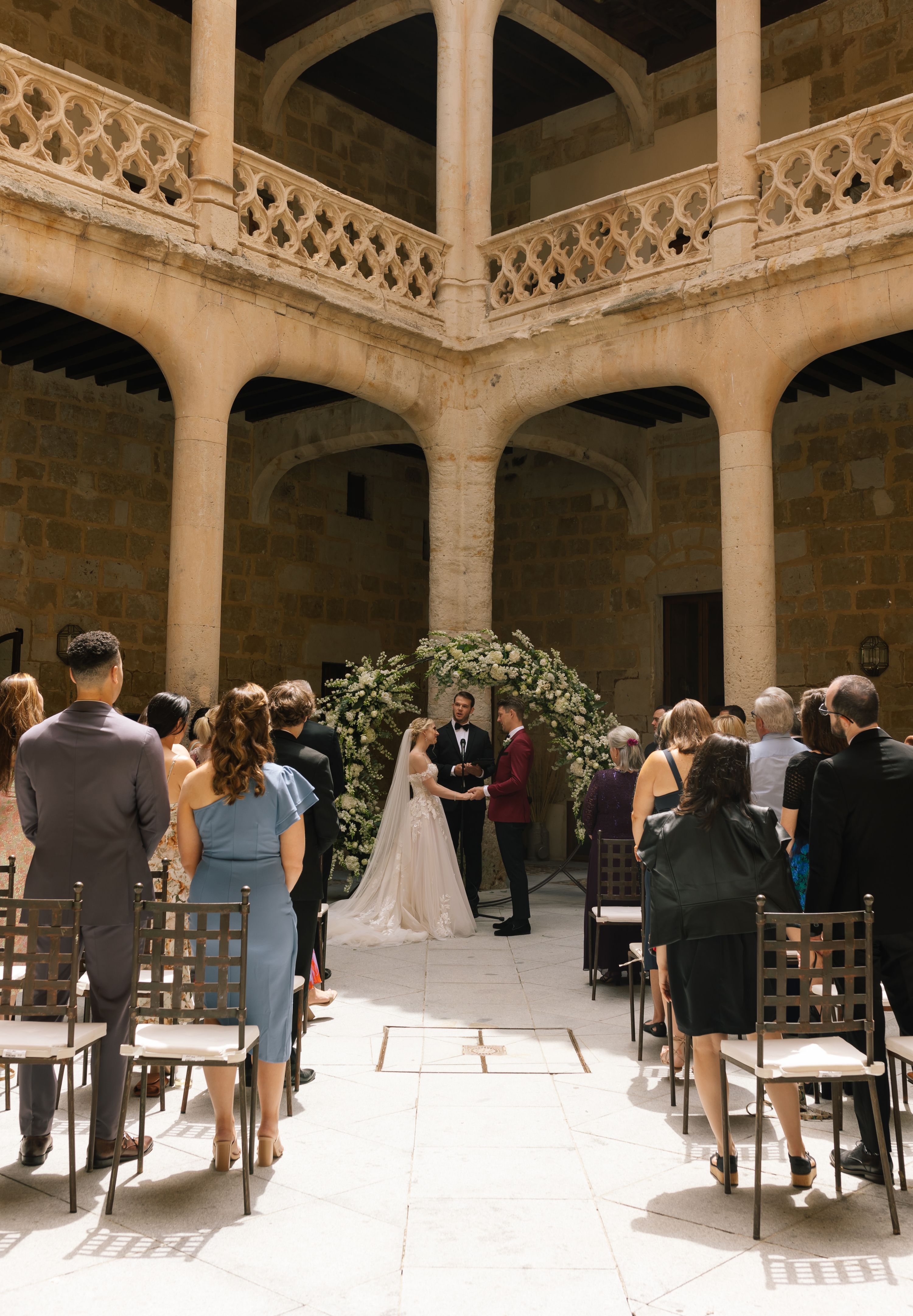 Bride and groom holds hands in front of their guests in a castle's courtyard during their destination wedding in Spain