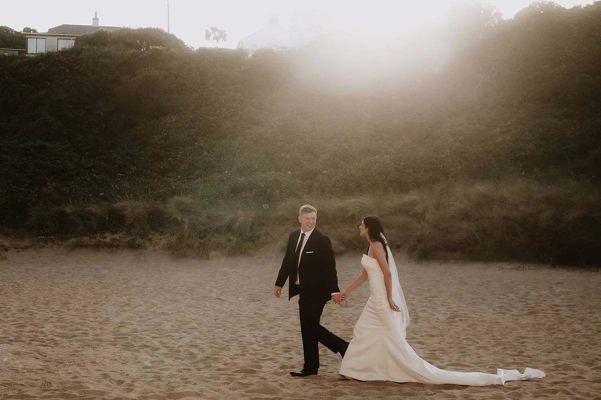 Newlyweds having a photoshoot at Antrim's white beach in summer after the ceremony of their destination wedding in Ireland