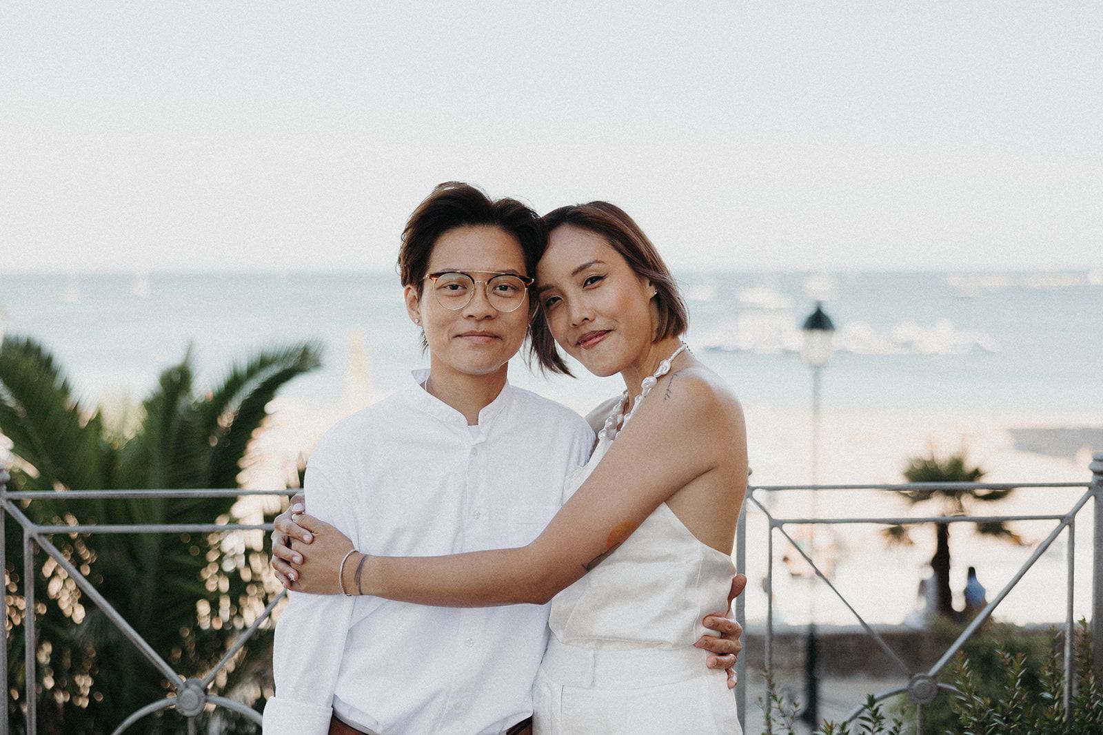 Same-sex couple dressed in white hugging with the sea in the background in Portugal