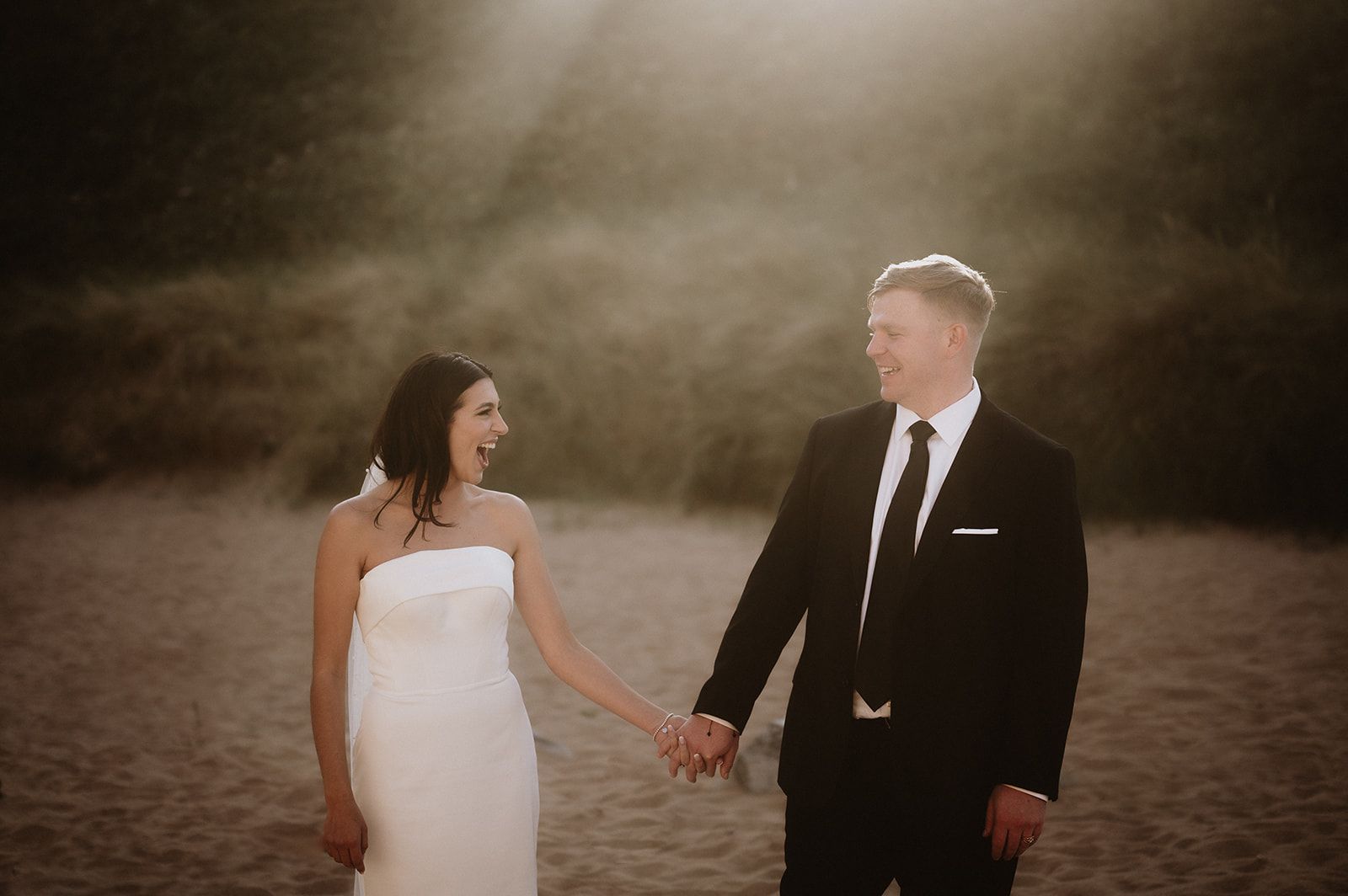 Happy newlyweds holding each other with rays of sun above in a beach in Northern Ireland