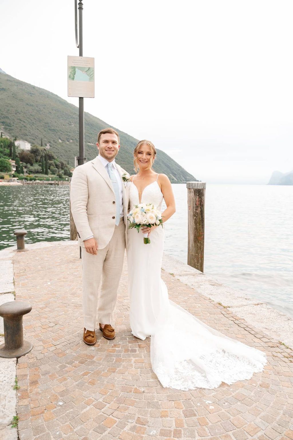 Bride and groom look at the camera with Lake Garda and a mountain in the background during their elopement in Italy