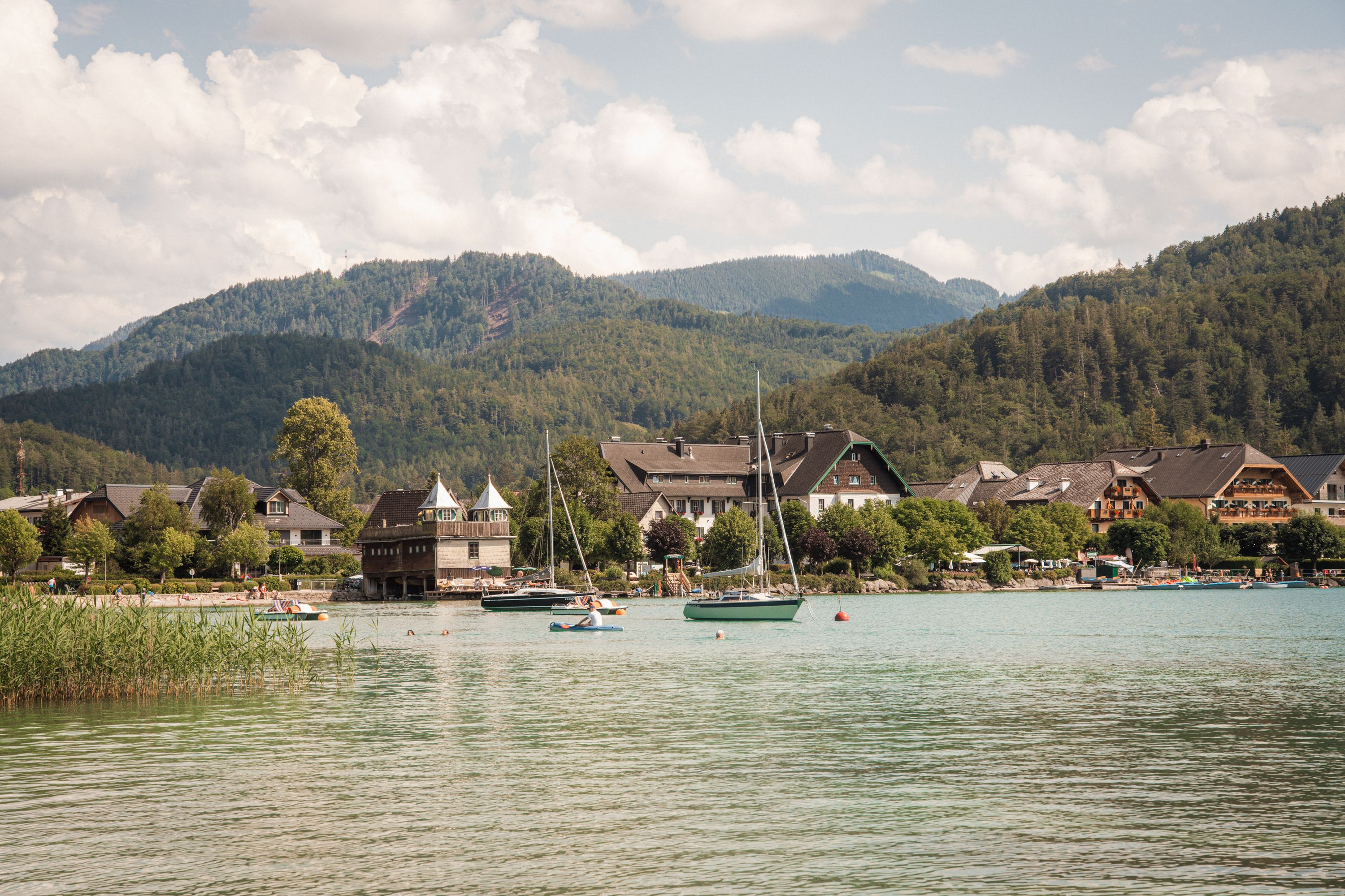 Sailboats on a clear Alpine lake ringed by forested hills in Austria's lake district