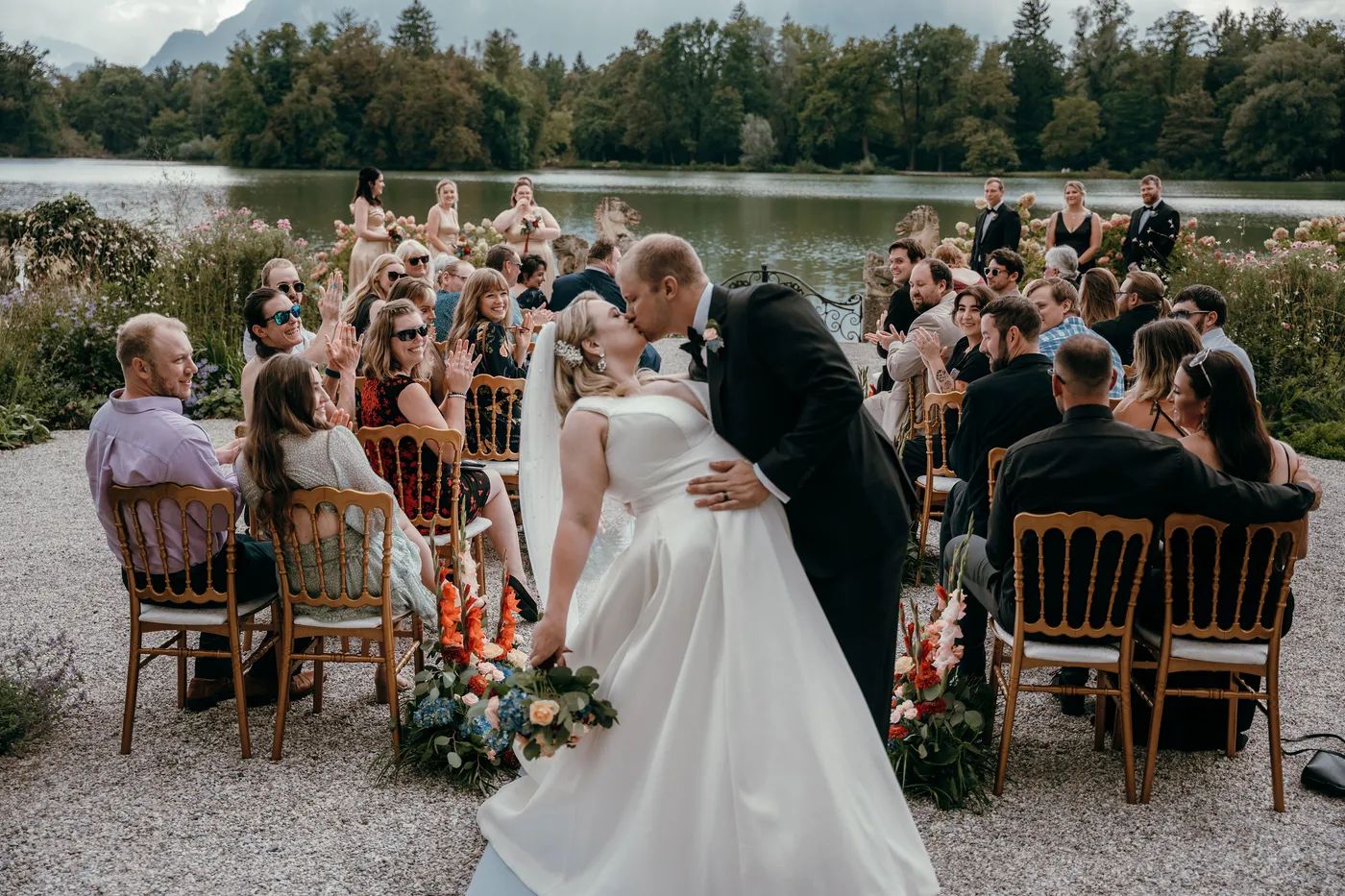 Newlyweds kiss in the aisle at their lakeside wedding near Salzburg as guests applaud