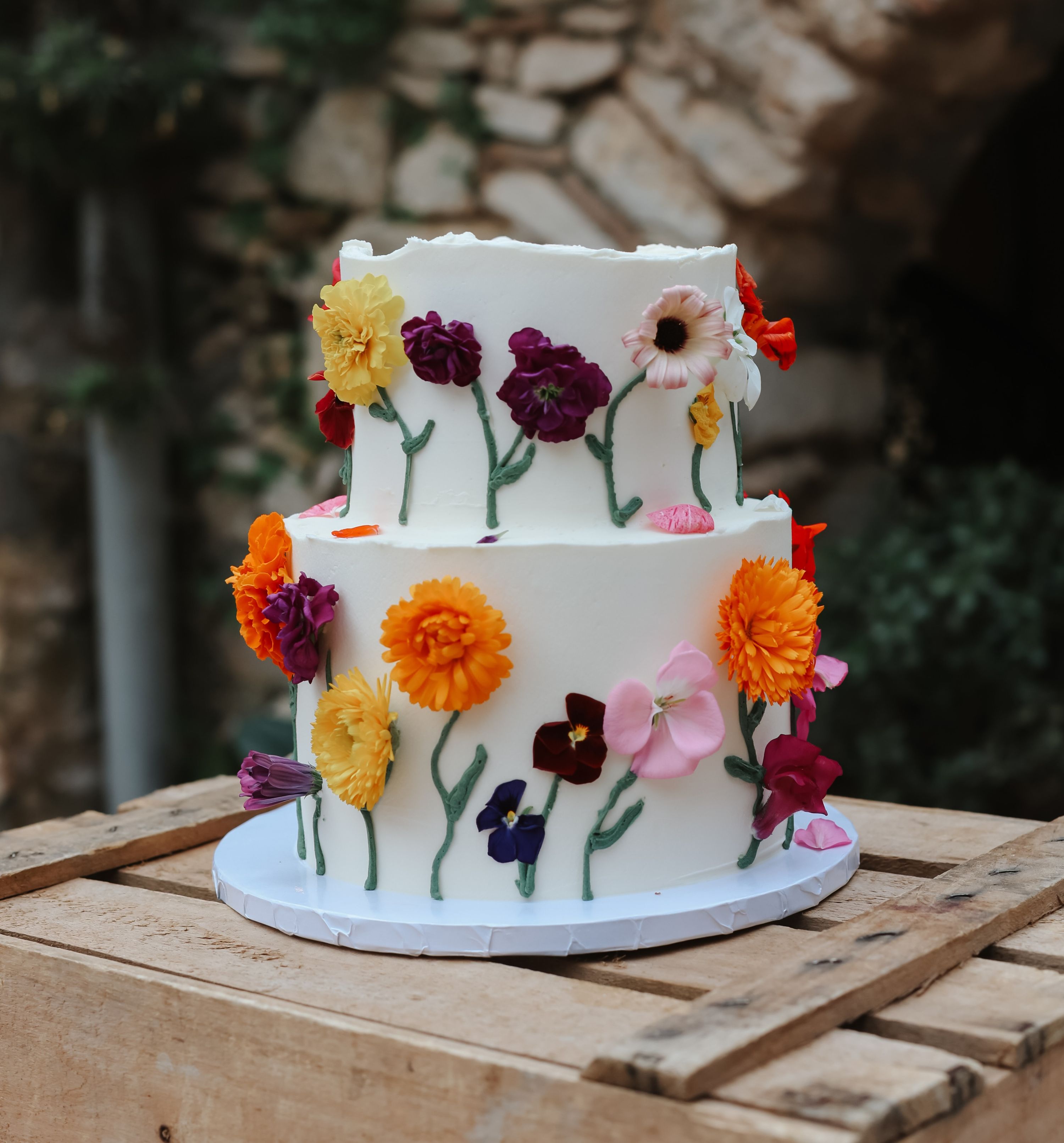 A 2-tiered white wedding cake with candy flowers of different colors all around