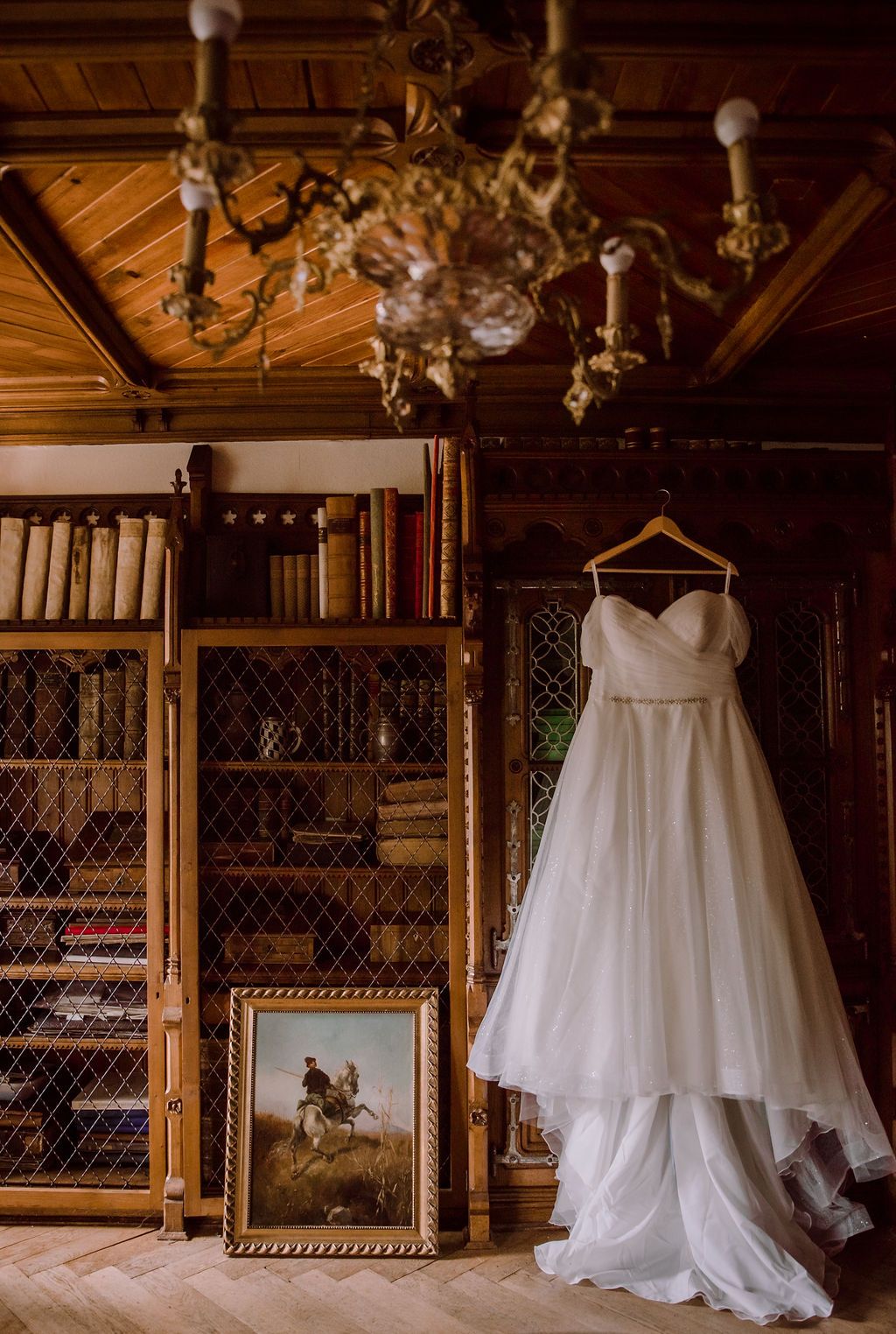 A wedding dress hanging inside a room with a chandelier and a bookcase for a couple about to have an elopement in Germany