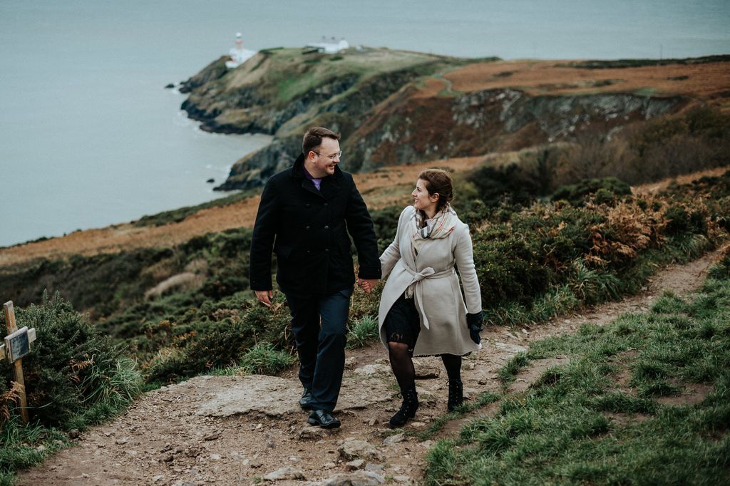 A couple in casual wear walks atop a cliff in Ireland with the Atlantic Ocean in the background