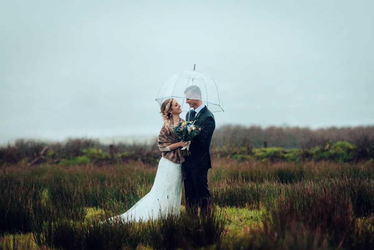 Bride and groom hold an umbrella during the photoshoot of their winter destination wedding in Ireland at the Dingle Peninsula
