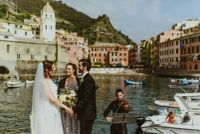 Couple having a ceremony outdoors in Cinque Terre by the river with a celebrant and a musician in front of them