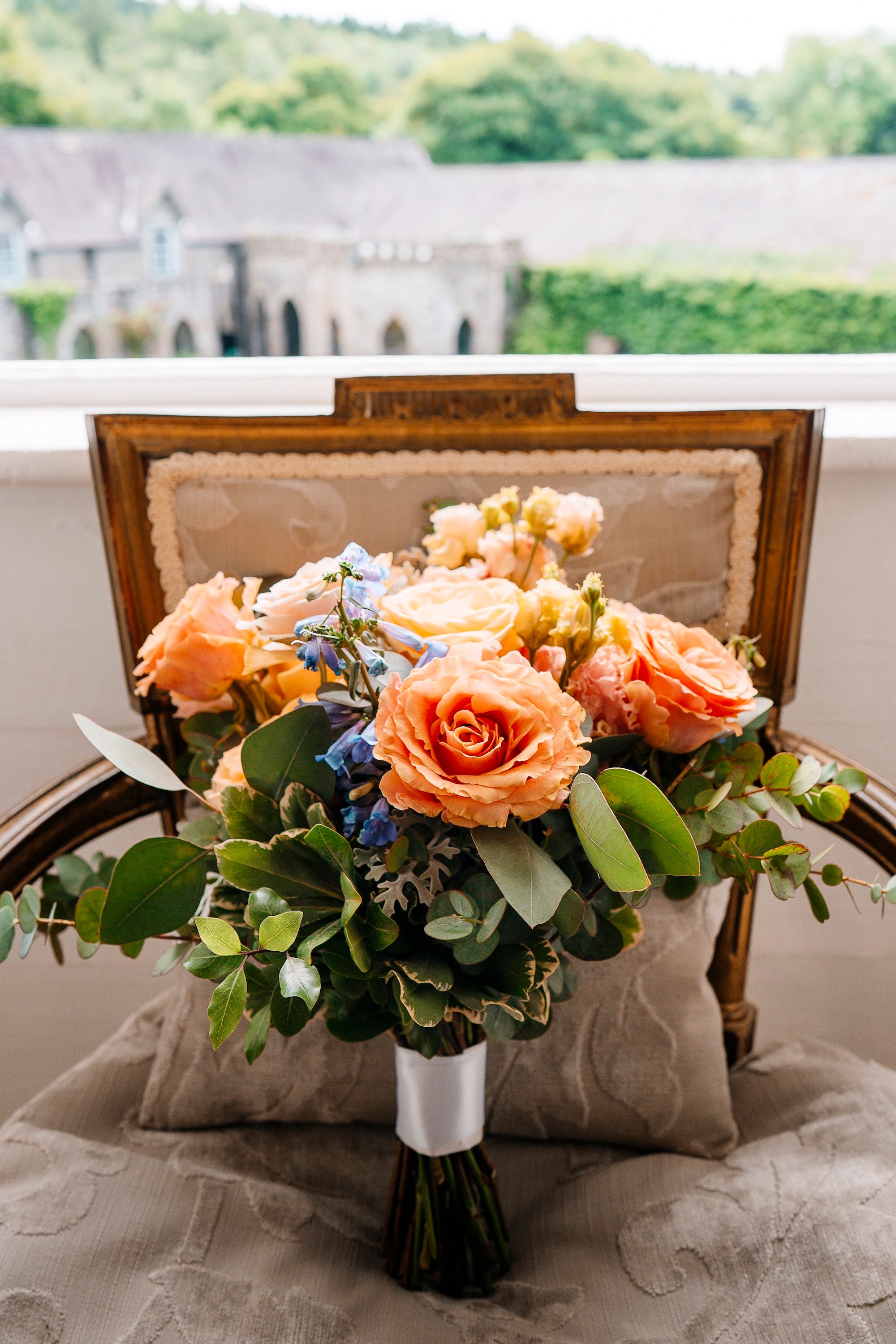 Bridal bouquet with peach and orange flowers, tiny blue flower additions, and green leaves at the bottom
