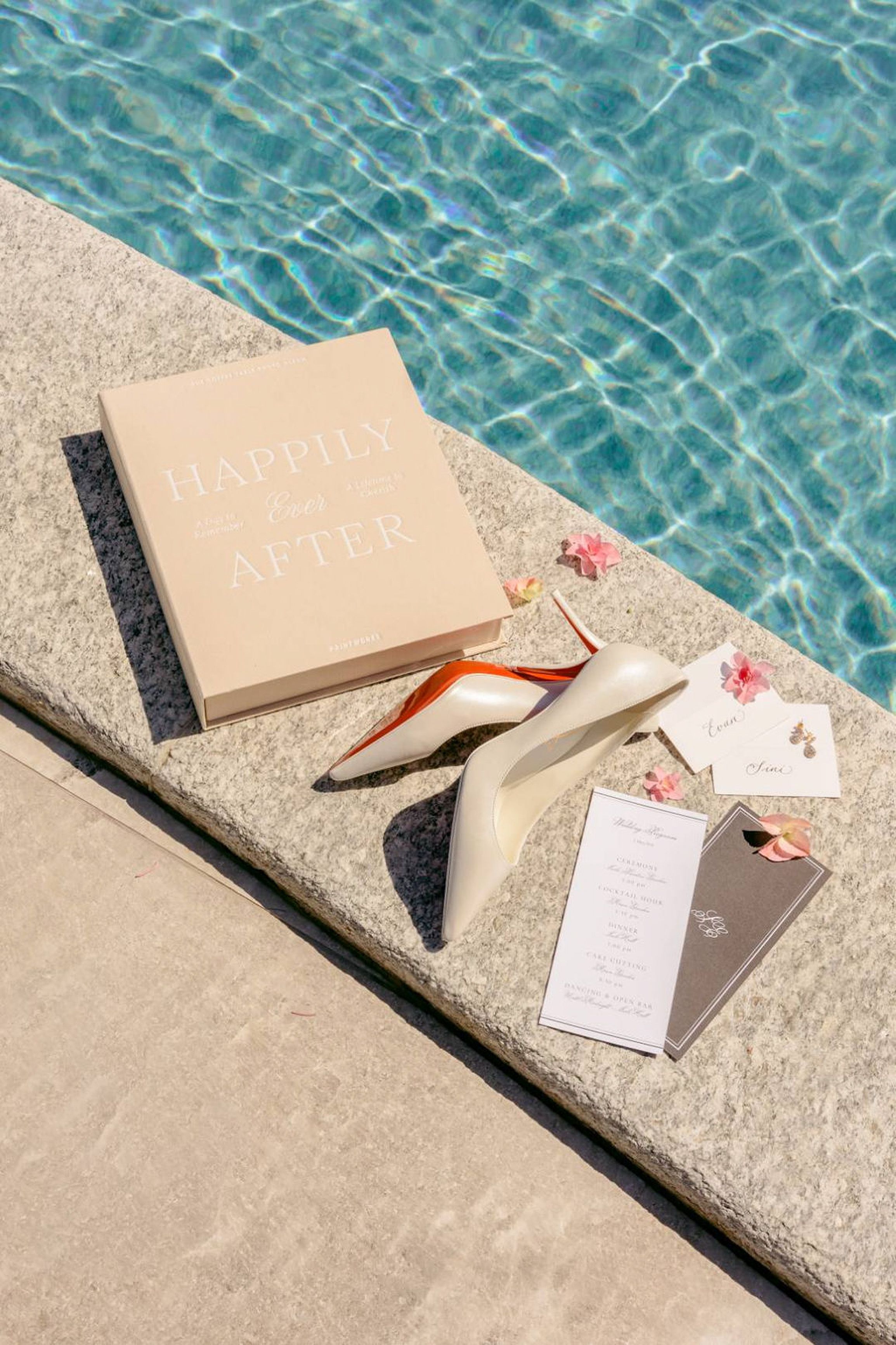 Wedding details by a pool with invitation suite, bridal shoes, and keepsake book for a small wedding in Italy