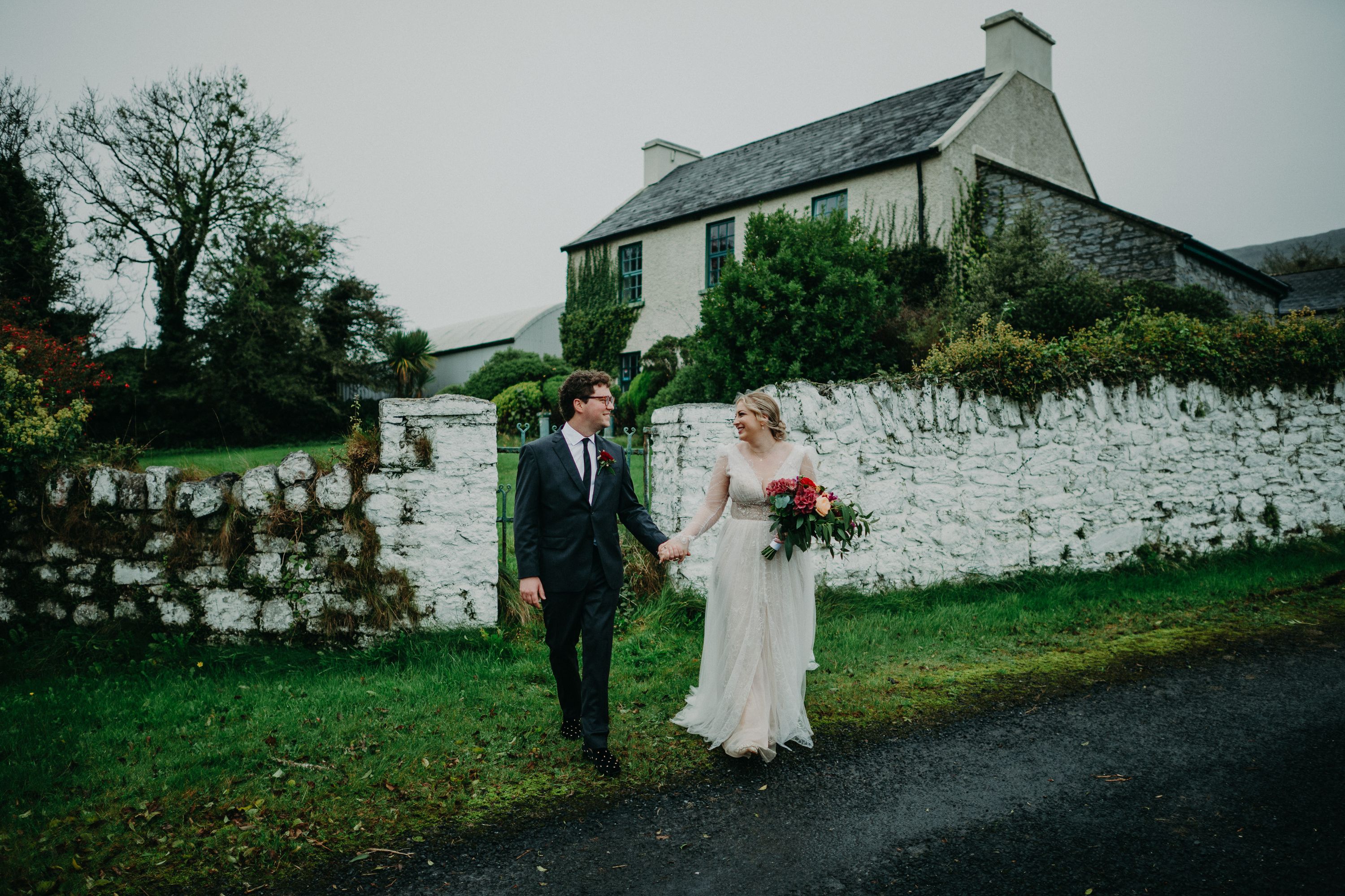 Newlyweds holding hands outside a stone cottage during a small wedding in Ireland