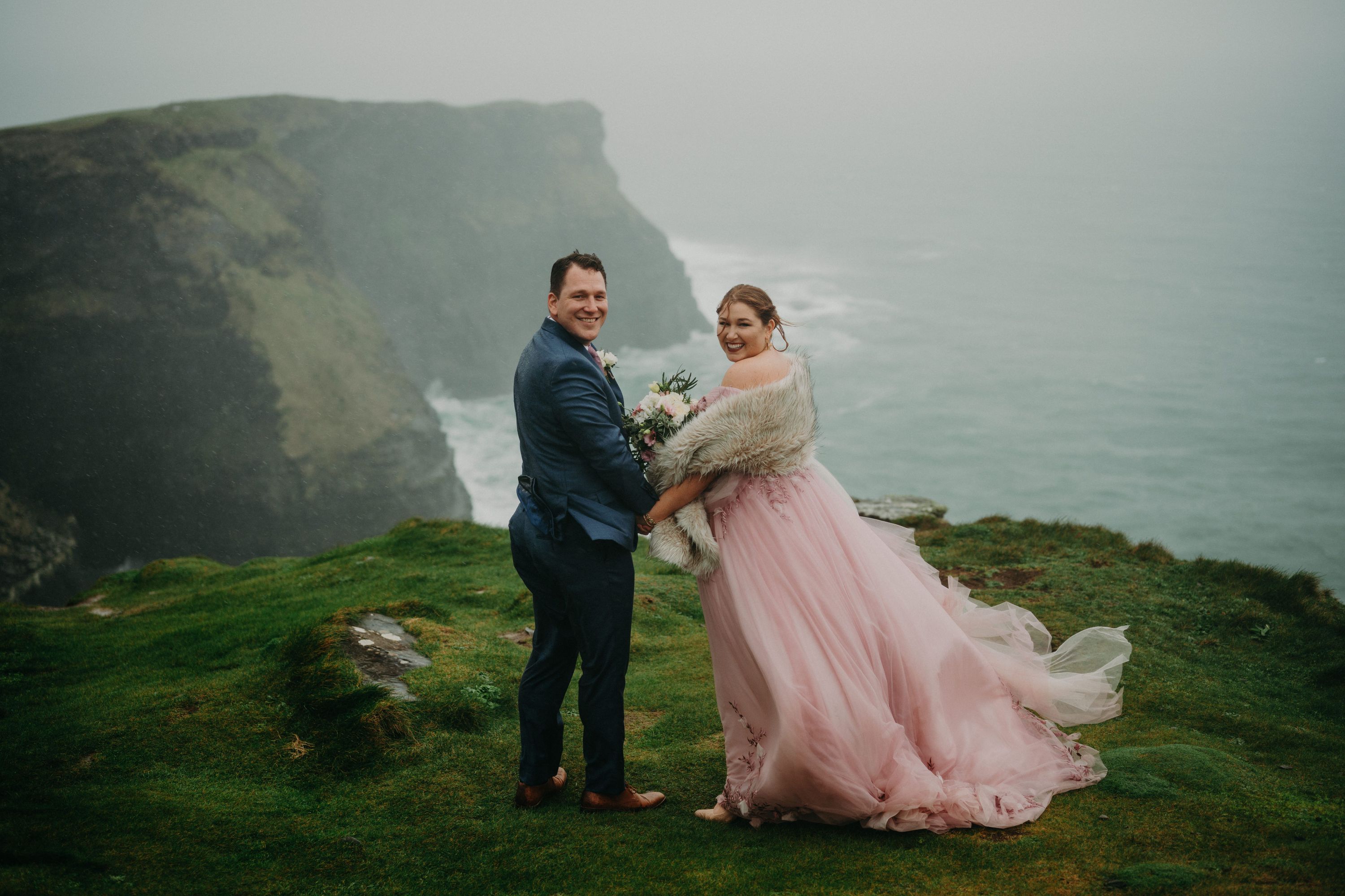 Bride in a pink dress with her groom renewing vows on the Cliffs of Moher
