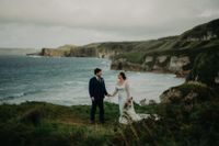 Bride and groom holding hands on the clifftop of Antrim during the photoshoot of their micro destination wedding in Ireland.