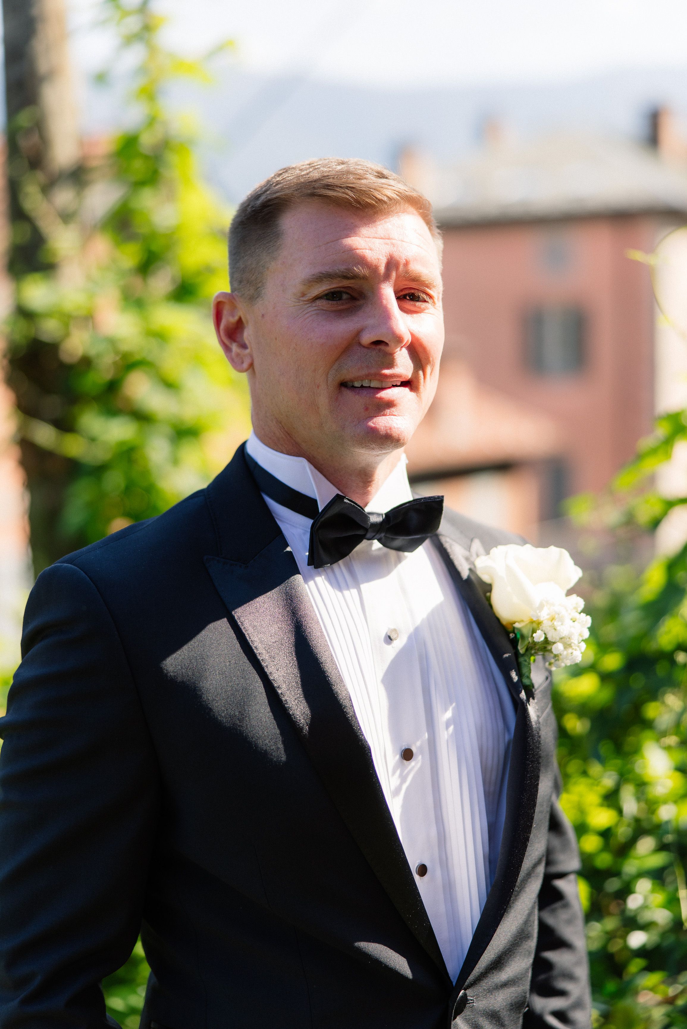 Groom in a black tuxedo standing in a garden with Lake Como views at a small wedding in Italy