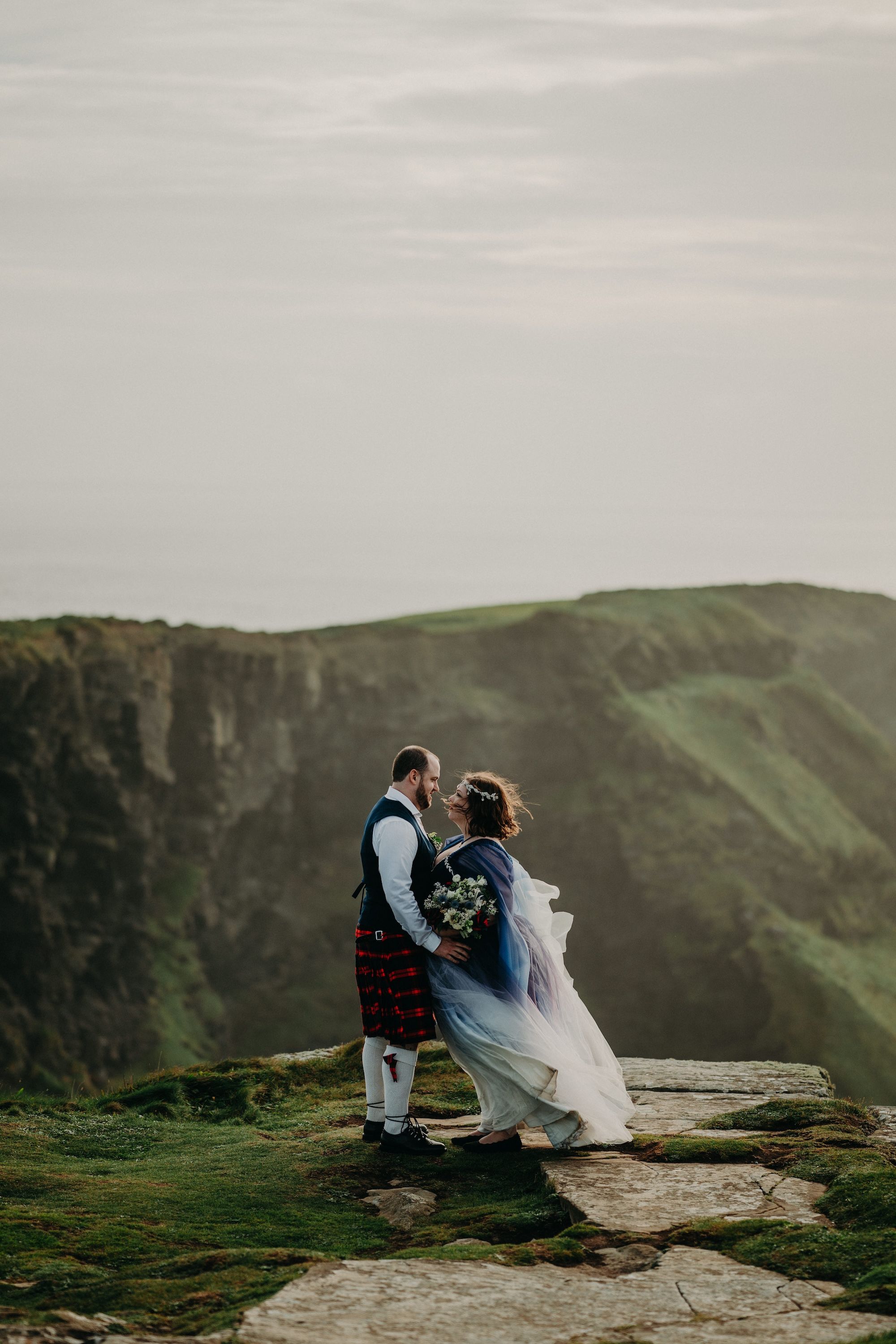 Newlyweds look at each other during the photoshoot of their Irish elopement with the Cliffs of Moher in the background