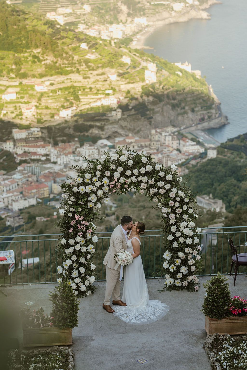 newlyweds kiss under a green and white arch when they eloped in Italy, with Amalfi views in the background