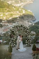 newlyweds kiss under a green and white arch when they eloped in Italy, with Amalfi views in the background