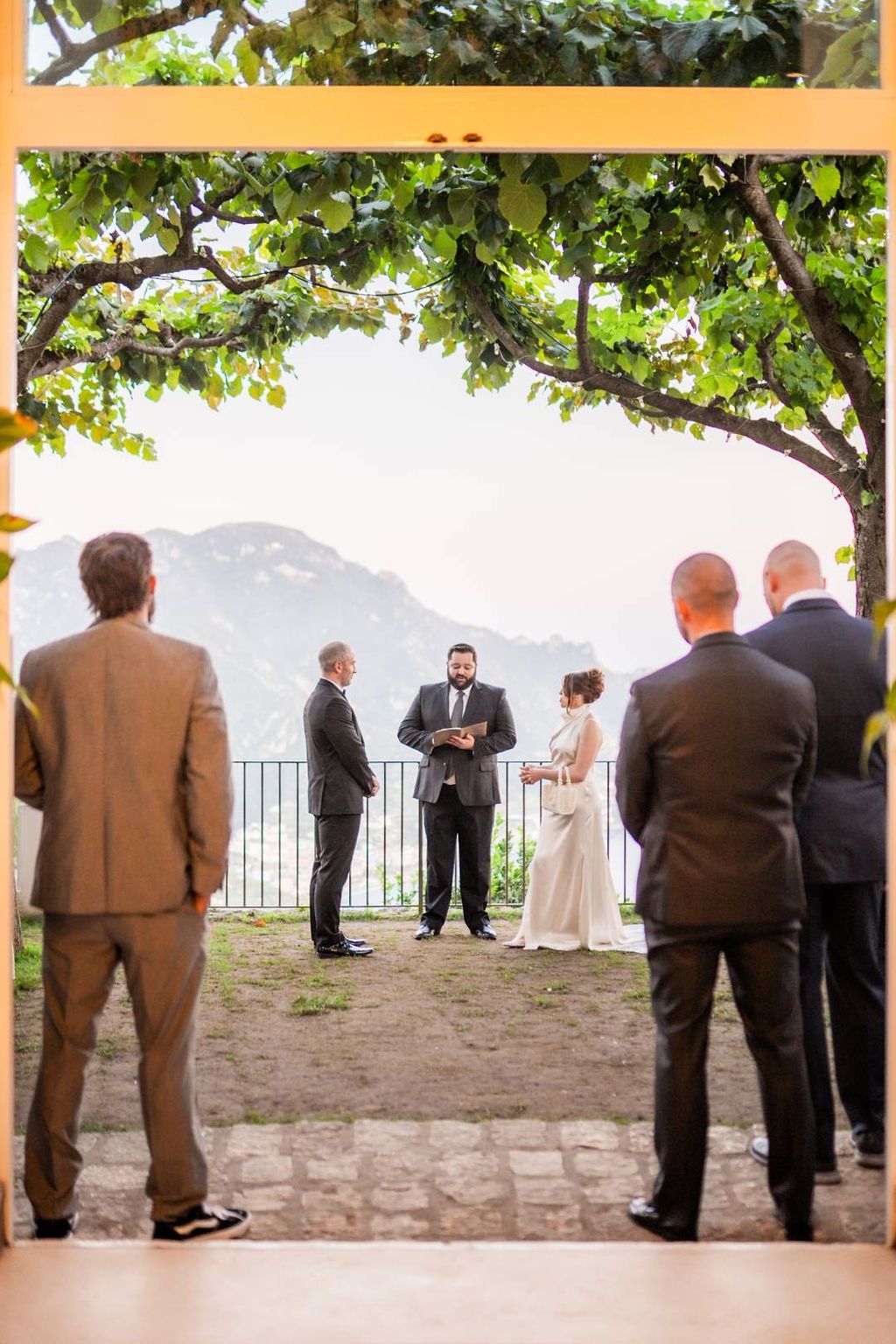 Bride and groom under the trees with Amalfi Coast in the background during the ceremony of their vow renewal in Italy