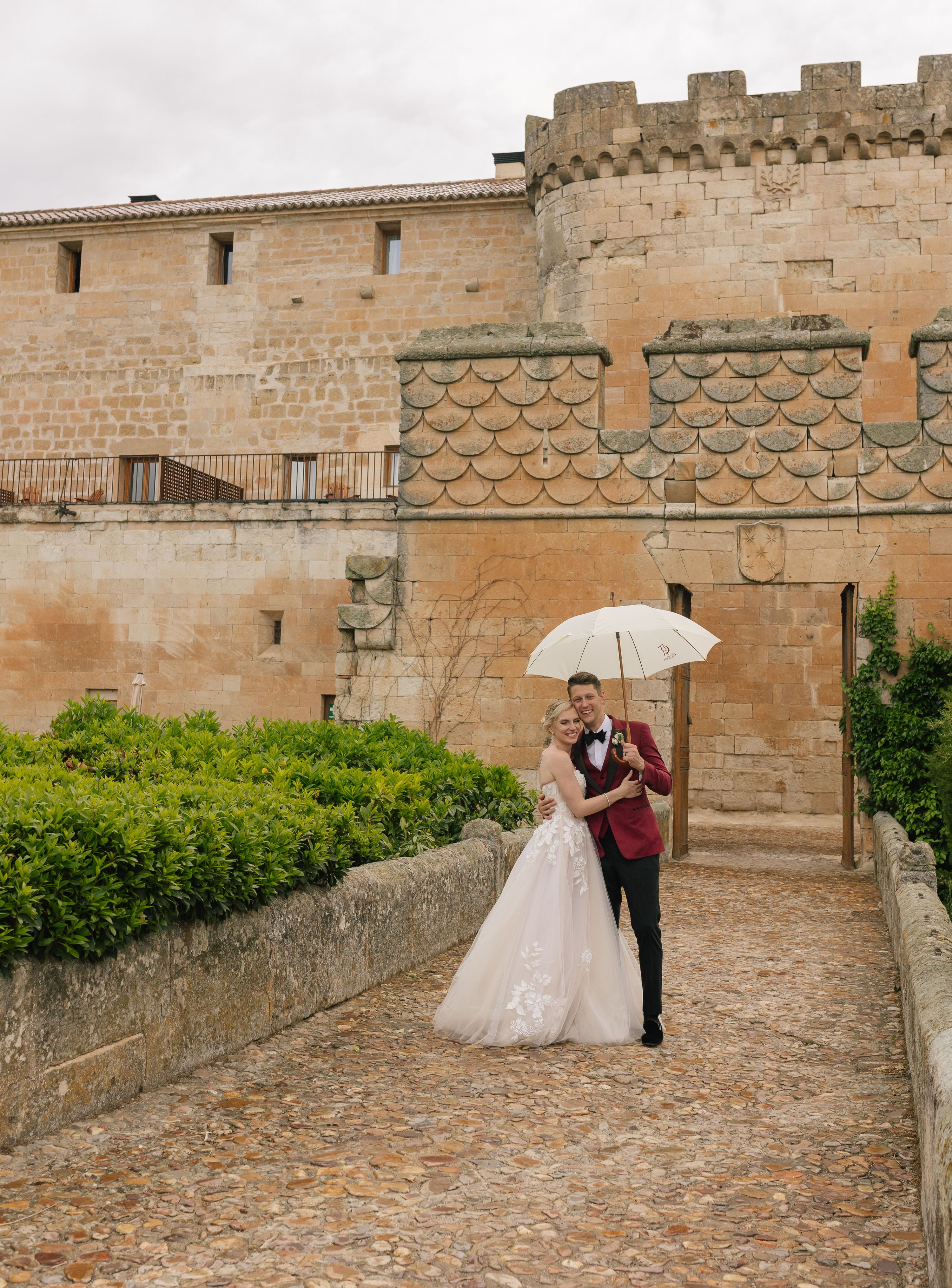 Bride and groom under a white umbrella as they stroll through the castle grounds when they got married in Spain