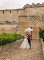 Bride and groom under a white umbrella as they stroll through the castle grounds when they got married in Spain