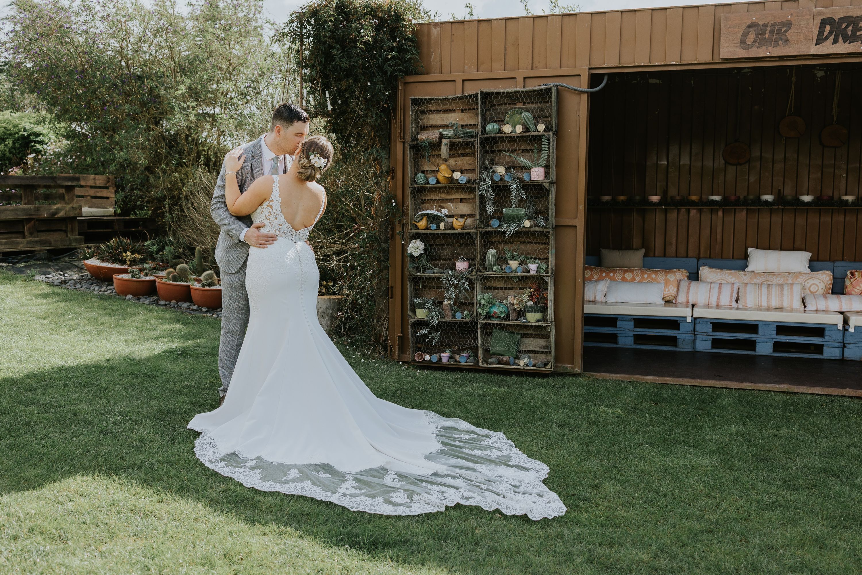Bride and groom hug outdoors at a grassy area  in front of an open wooden cabin during their destination wedding in Portugal
