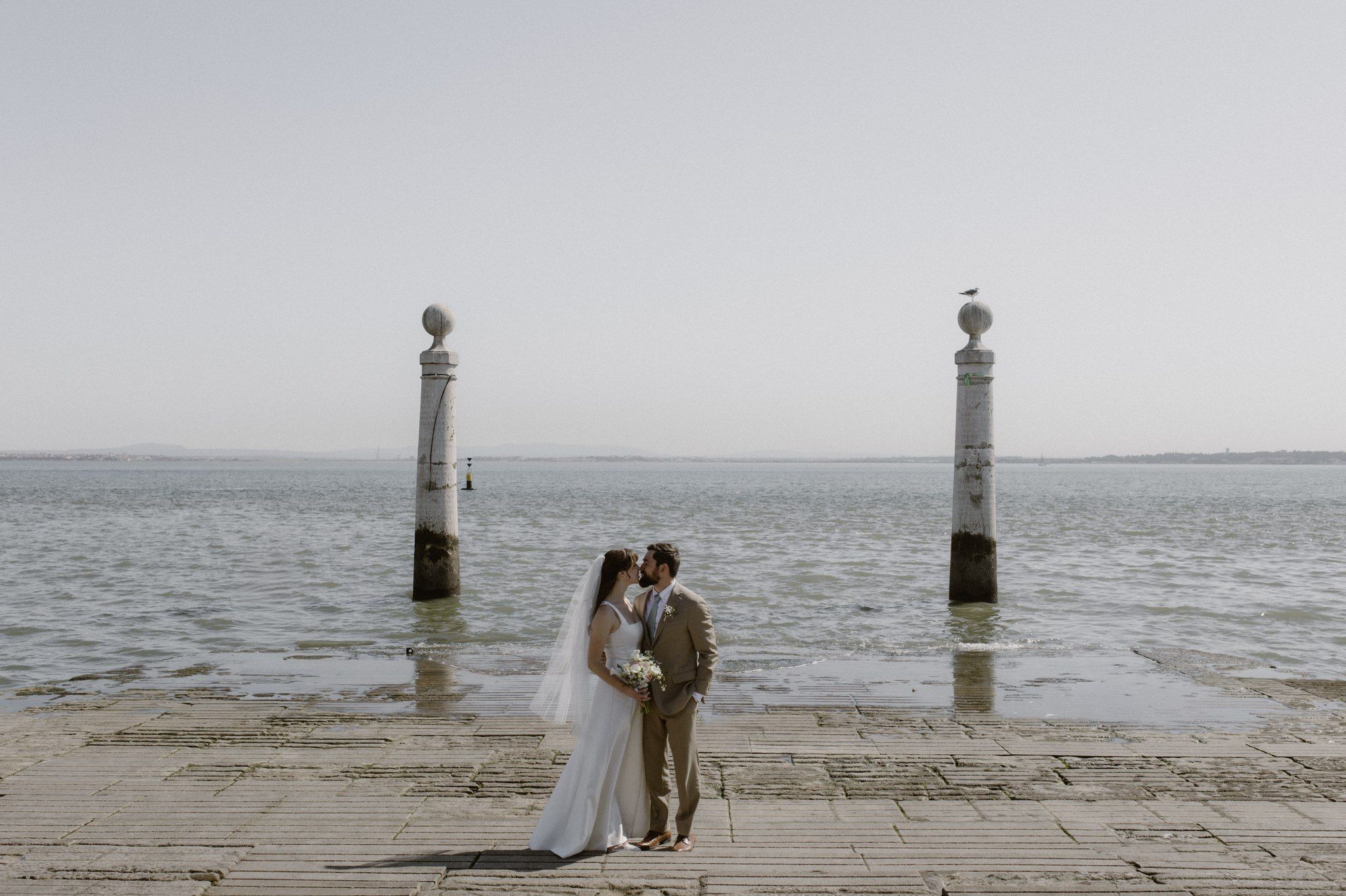 Bride and groom kiss on the shores of a beach in the city center of Lisbon for their small wedding in Portugal