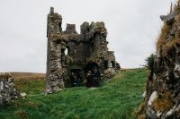 A castle ruin perched atop the lush green meadows of the hills in Kerry