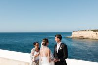 Bride and groom holds hands on a clifftop spot under the clear summer skies of Algarve during their Portuguese wedding abroad