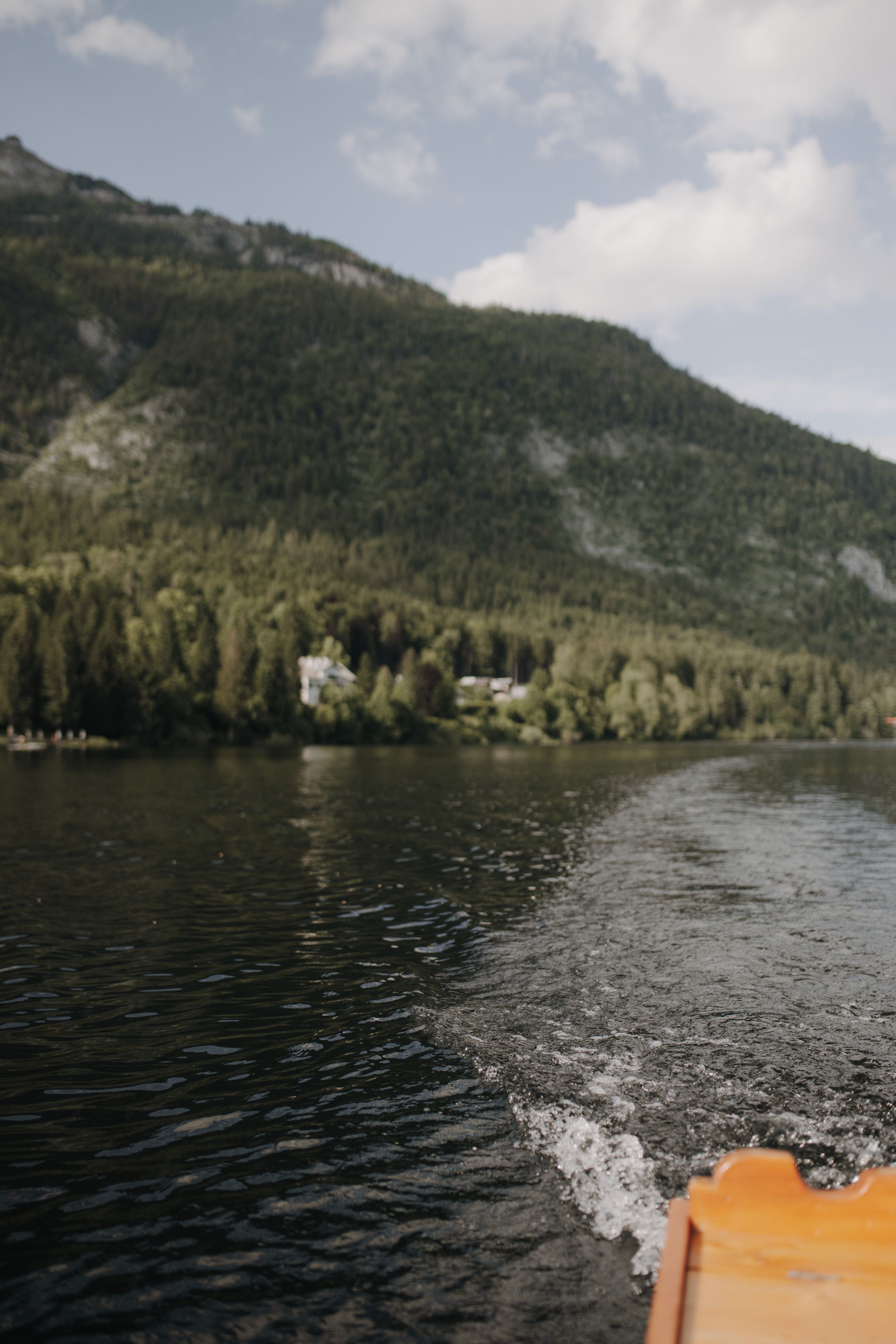 Crossing a dark Alpine lake by wooden boat, forested slopes ahead