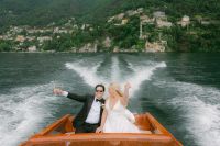 Newlyweds on a boat sailing atop Lake Como with views if the Como region and the lake at the back