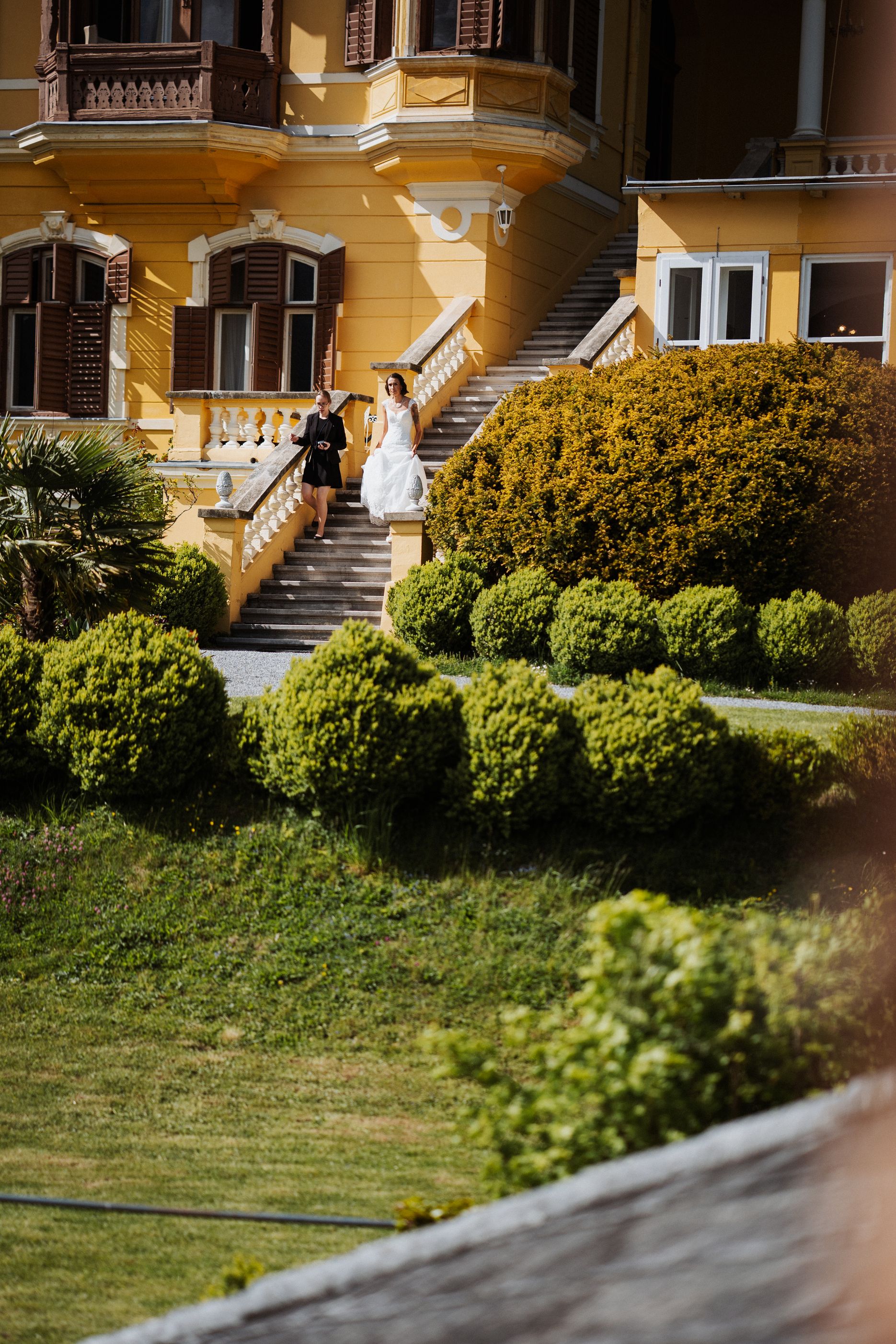 Bride descending the garden steps of a yellow lakeside villa in Carinthia
