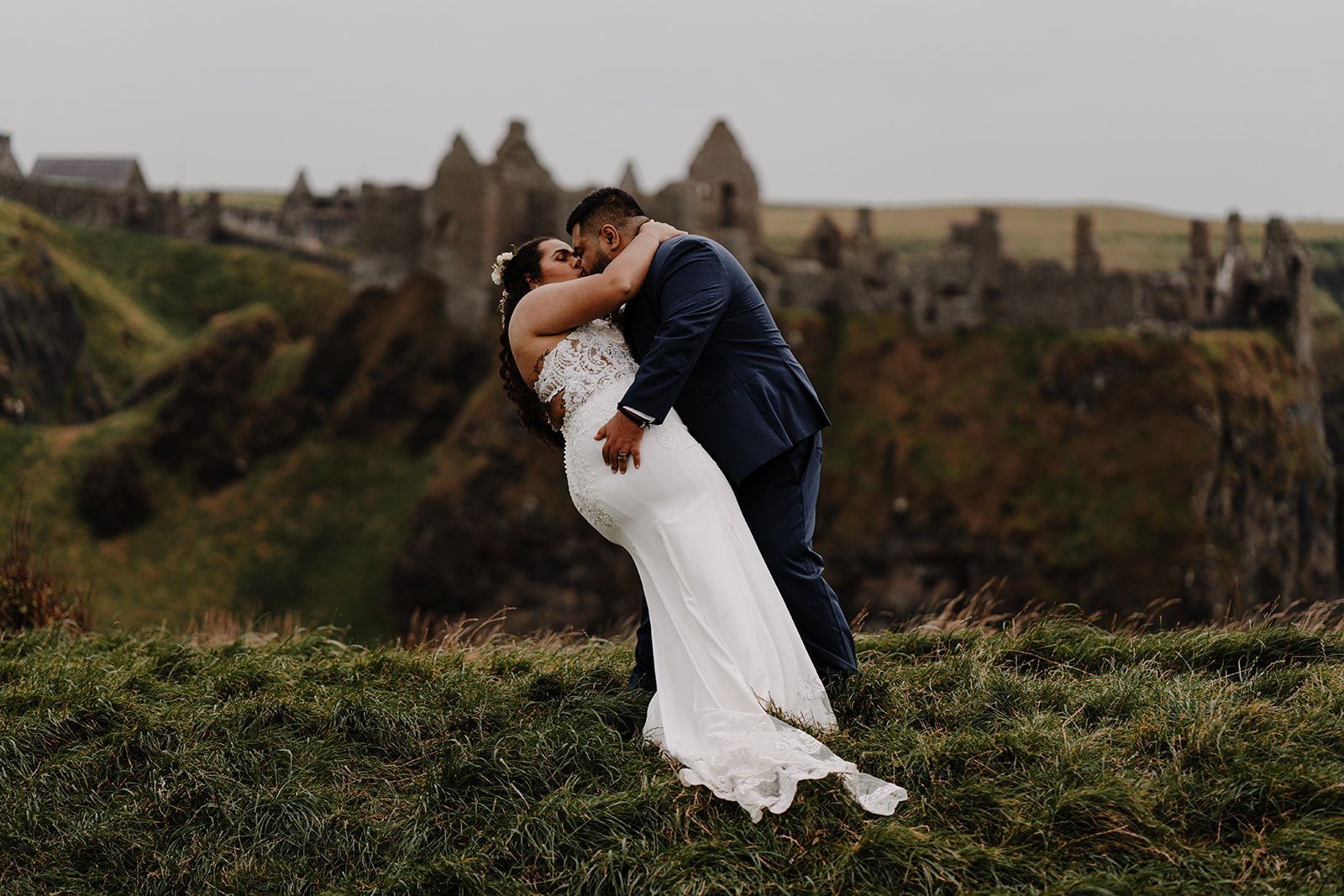 Bride and groom kissing atop a cliff in County Antrim with castle ruins in the background during their elopement in Ireland