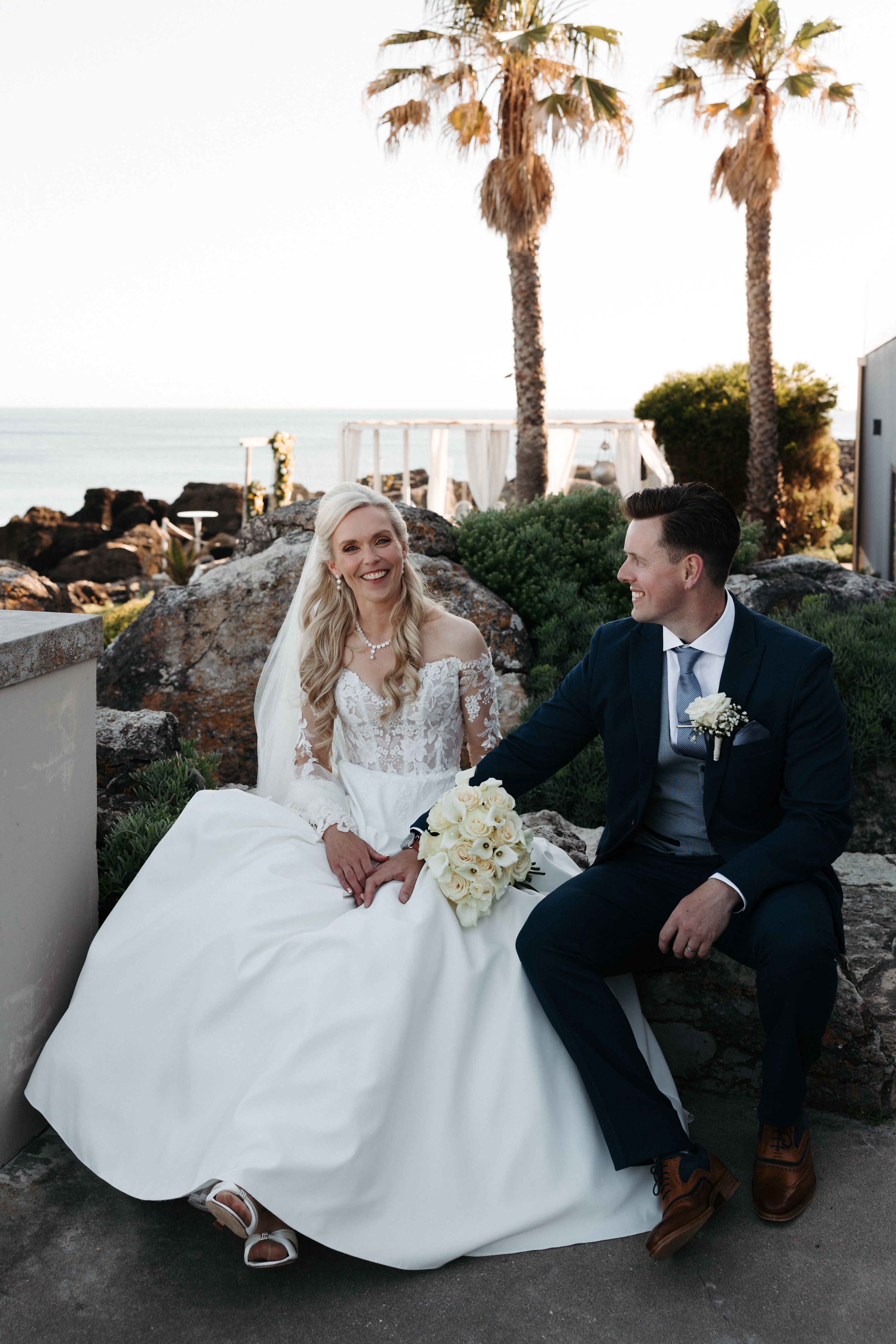 Groom looks at his bride with the beach and the Cascais coast in the background during their micro wedding in Portugal