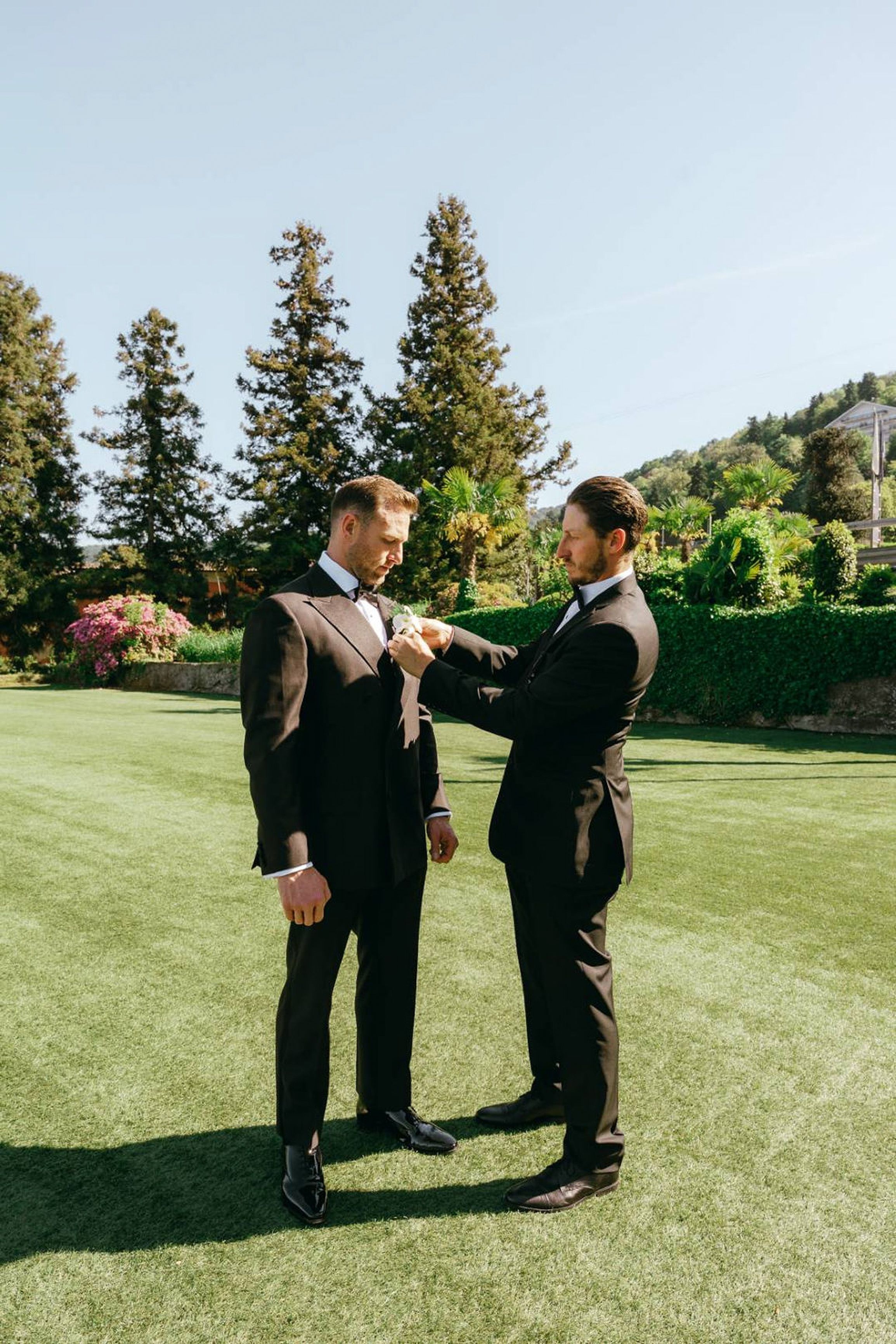 Groom adjusting his boutonniere with a groomsman in a garden setting for a small wedding in Italy