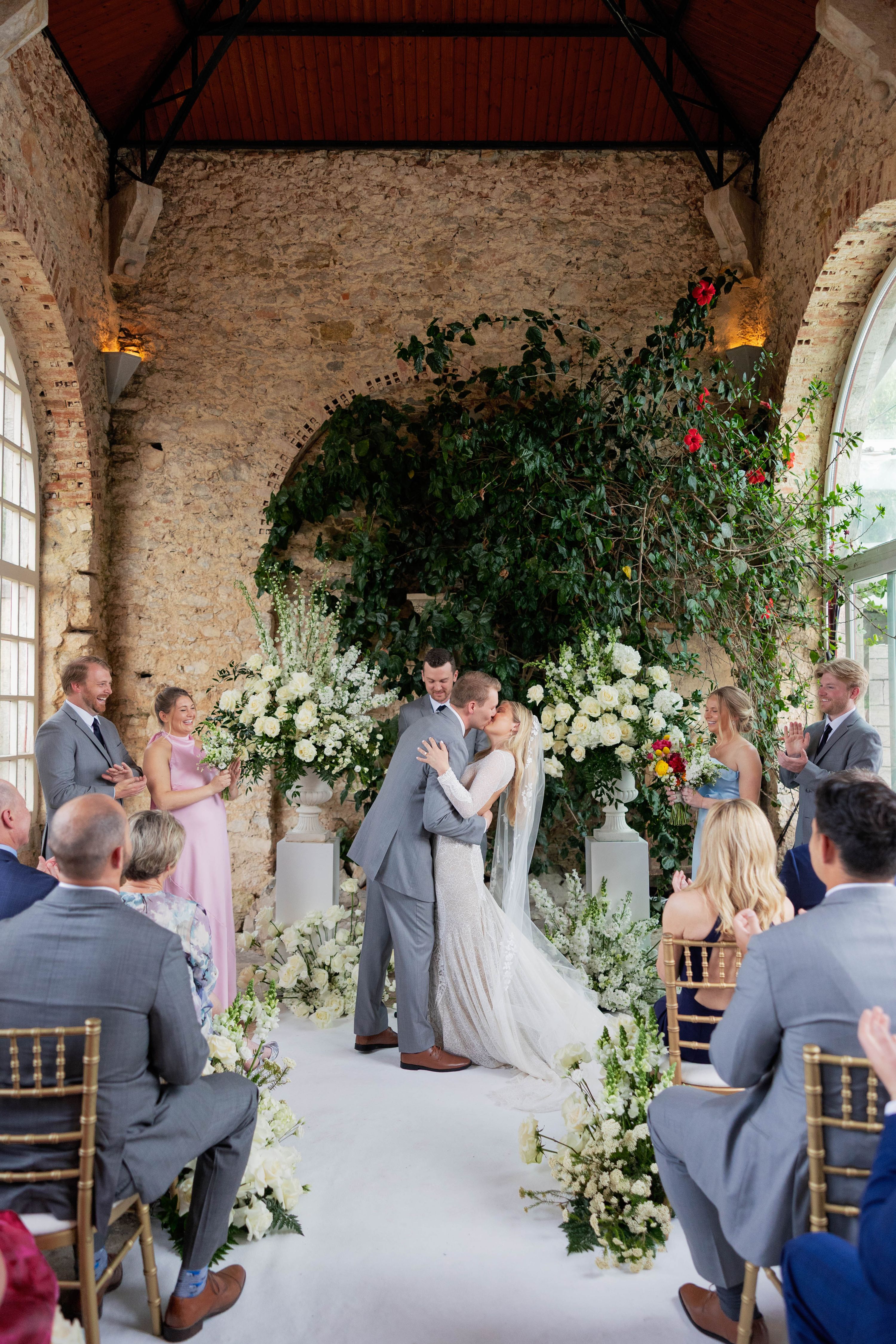 Bride and groom kissing in front of their guests inside a medieval walled event room in Portugal with huge windows