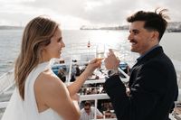 Couple holding glasses of champagne in a sailboat with their guests and Tagus river in the background