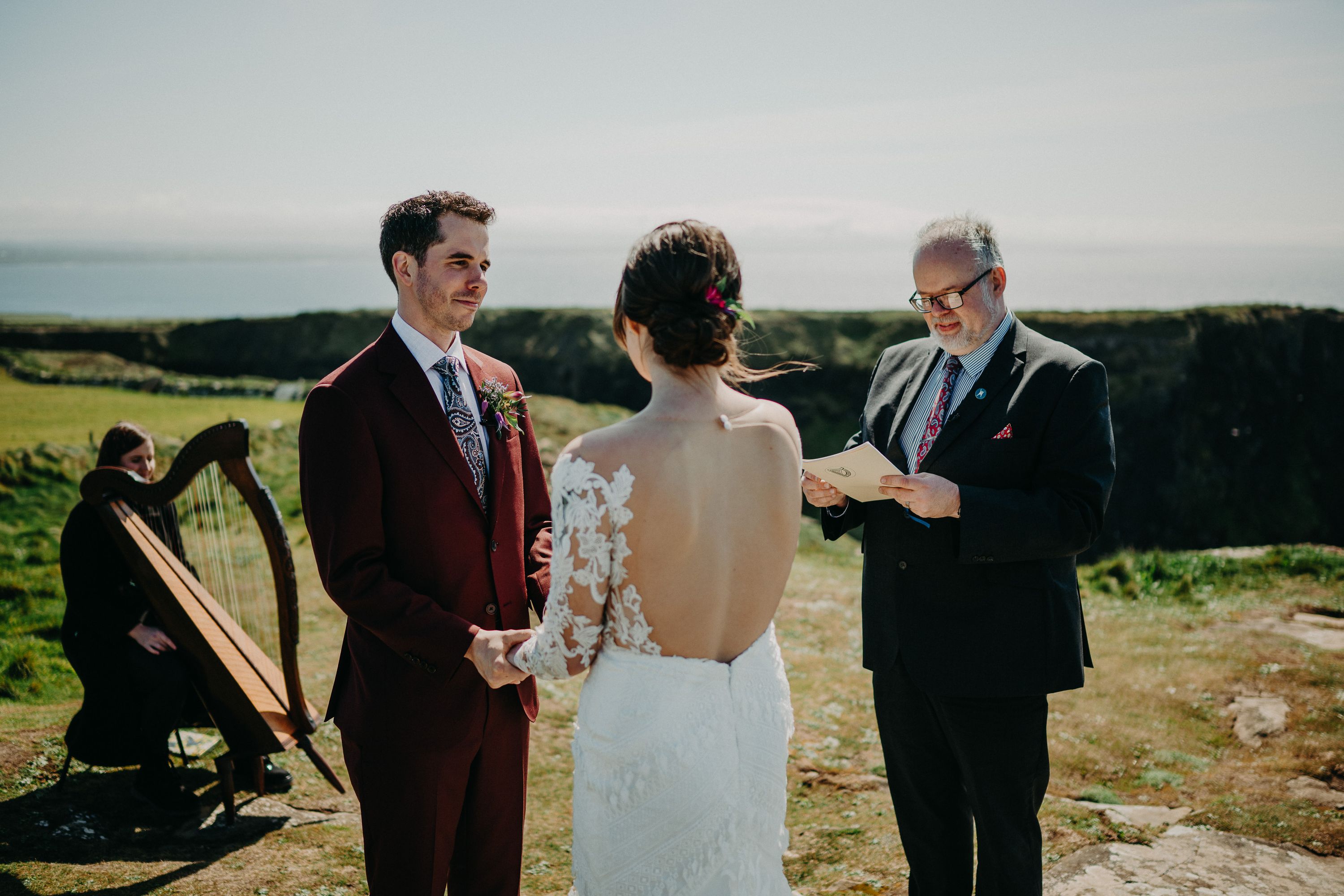 A ceremony with a musician playing a harp and an officiant handling the ceremony of a bride and groom having their intimate wedding in Ireland