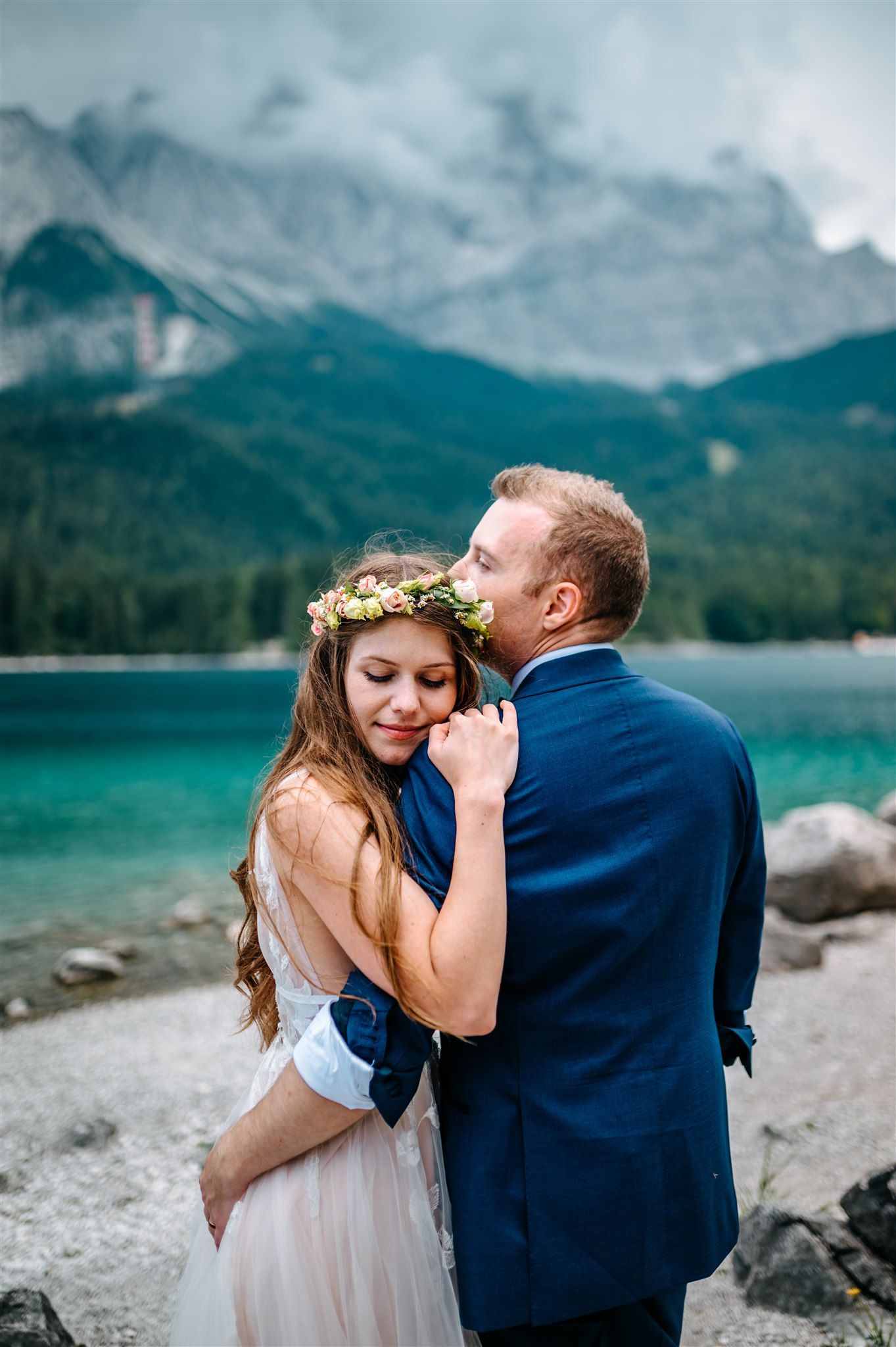 A groom kissing his bride with the lake and mountains behind them for their intimate wedding in Germany