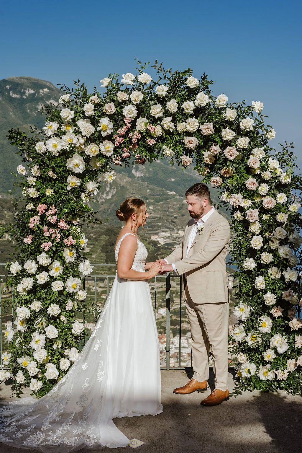 Bride and groom hold hands during the ceremony of their elopement in Italy atop a terrace with views of Amalfi