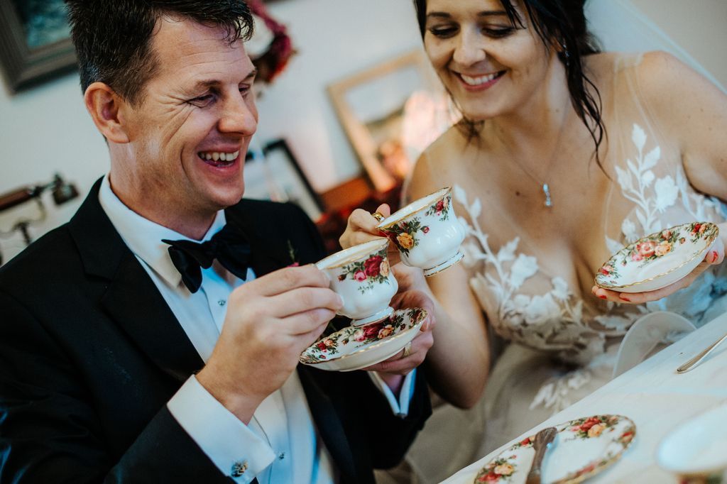 Bride and groom seated and doing a toast with their teacups as they smile during the celebration of their destination wedding in Ireland